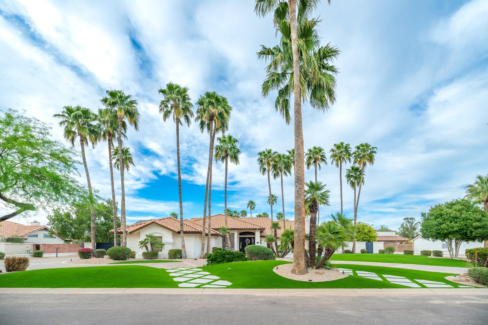 Stunning desert retreat framed by towering palms and manicured lawns, nestled in a peaceful residential neighborhood with spacious grounds and Spanish-style architecture.