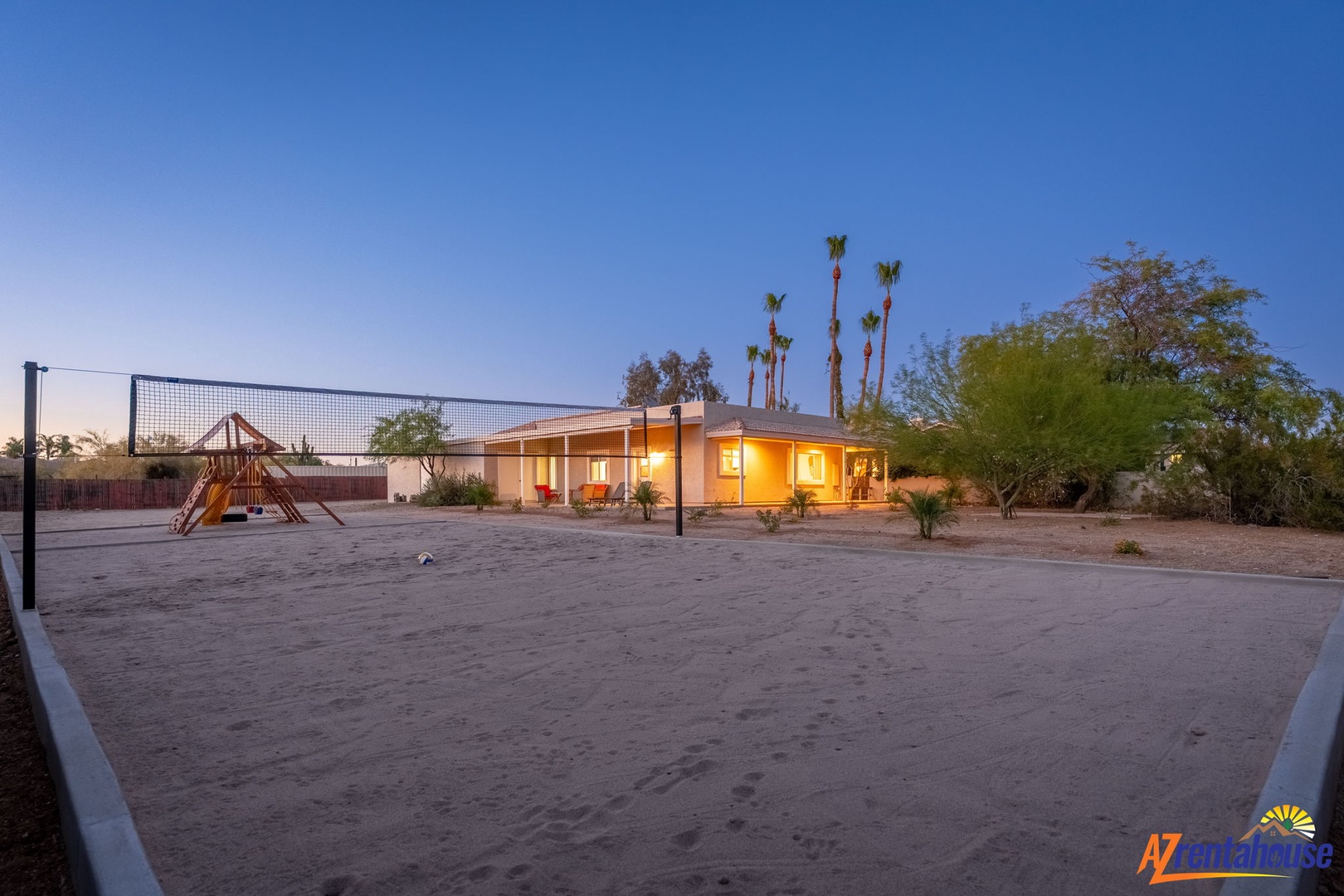 Desert oasis property with volleyball court and children's playground, set amid palm trees and natural landscaping against clear evening skies.