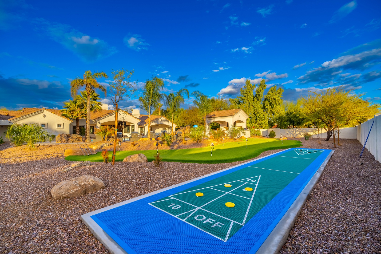 A spacious desert-inspired backyard with private putting green, shuffleboard court, and lush landscaping offers endless outdoor fun beneath sunny Arizona skies.