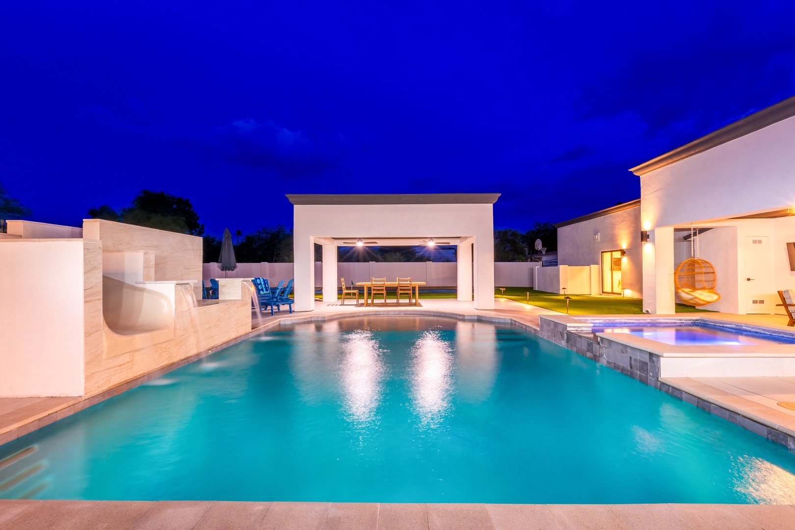 A luminous poolside retreat awaits under a twilight sky, with elegant white structures and warm lighting framing the serene turquoise waters and inviting outdoor spaces.
