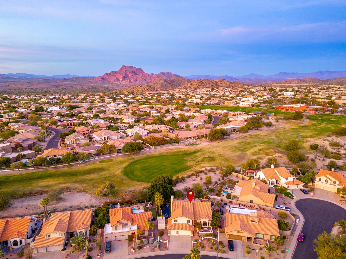 Aerial view of a desert golf course community with dramatic mountain backdrop and expansive southwestern landscape at dusk.
