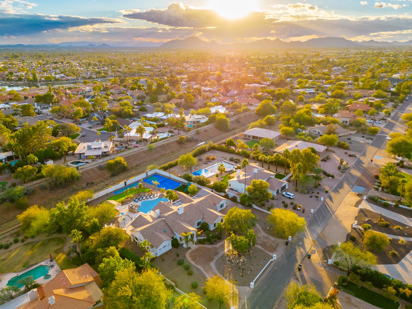 Aerial view of the property nestled in a serene residential neighborhood, with mountain backdrop and surrounding area bathed in golden sunset light.