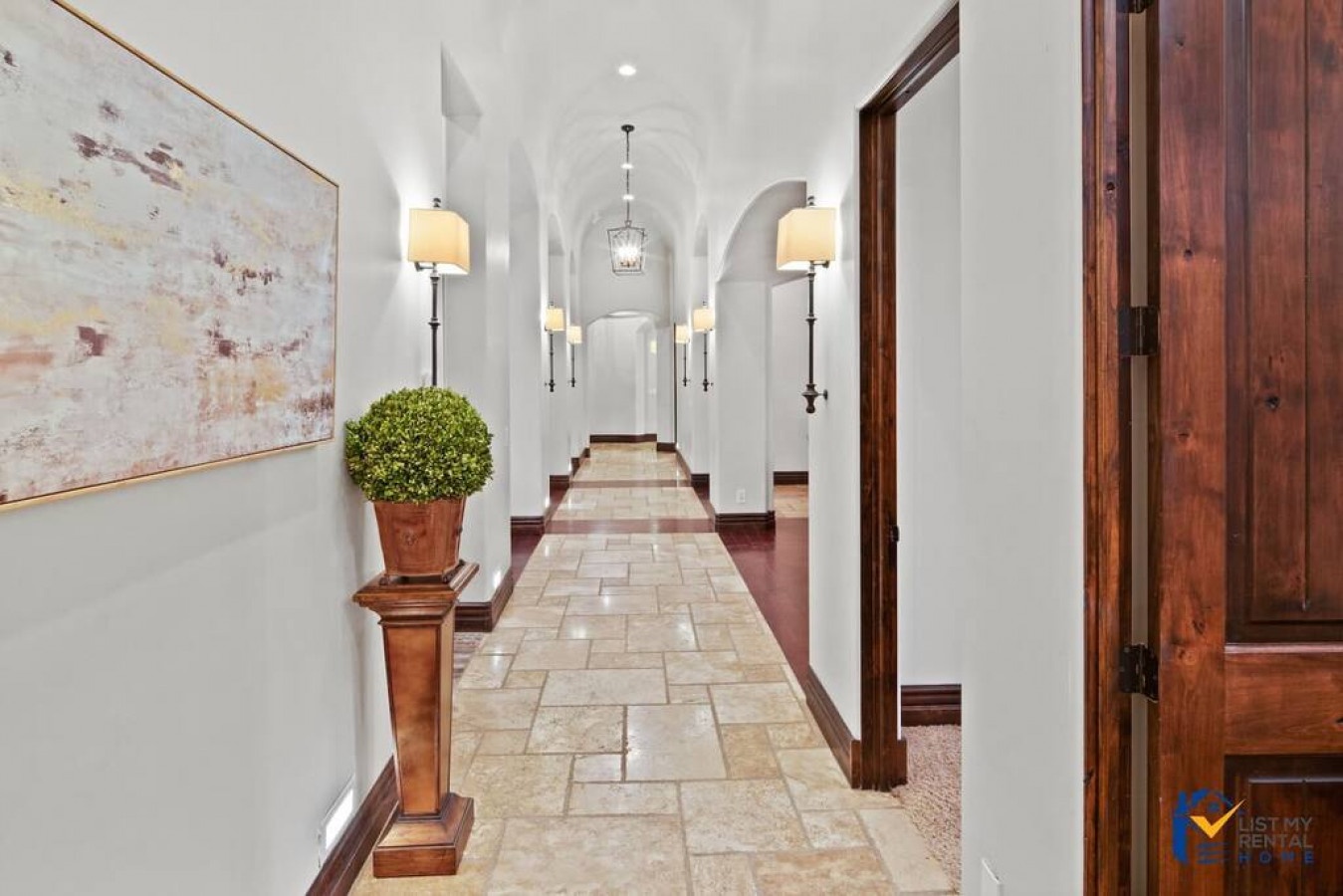 Step into this elegant hallway where warm sconces cast a gentle glow over stone floors and rich wood accents.