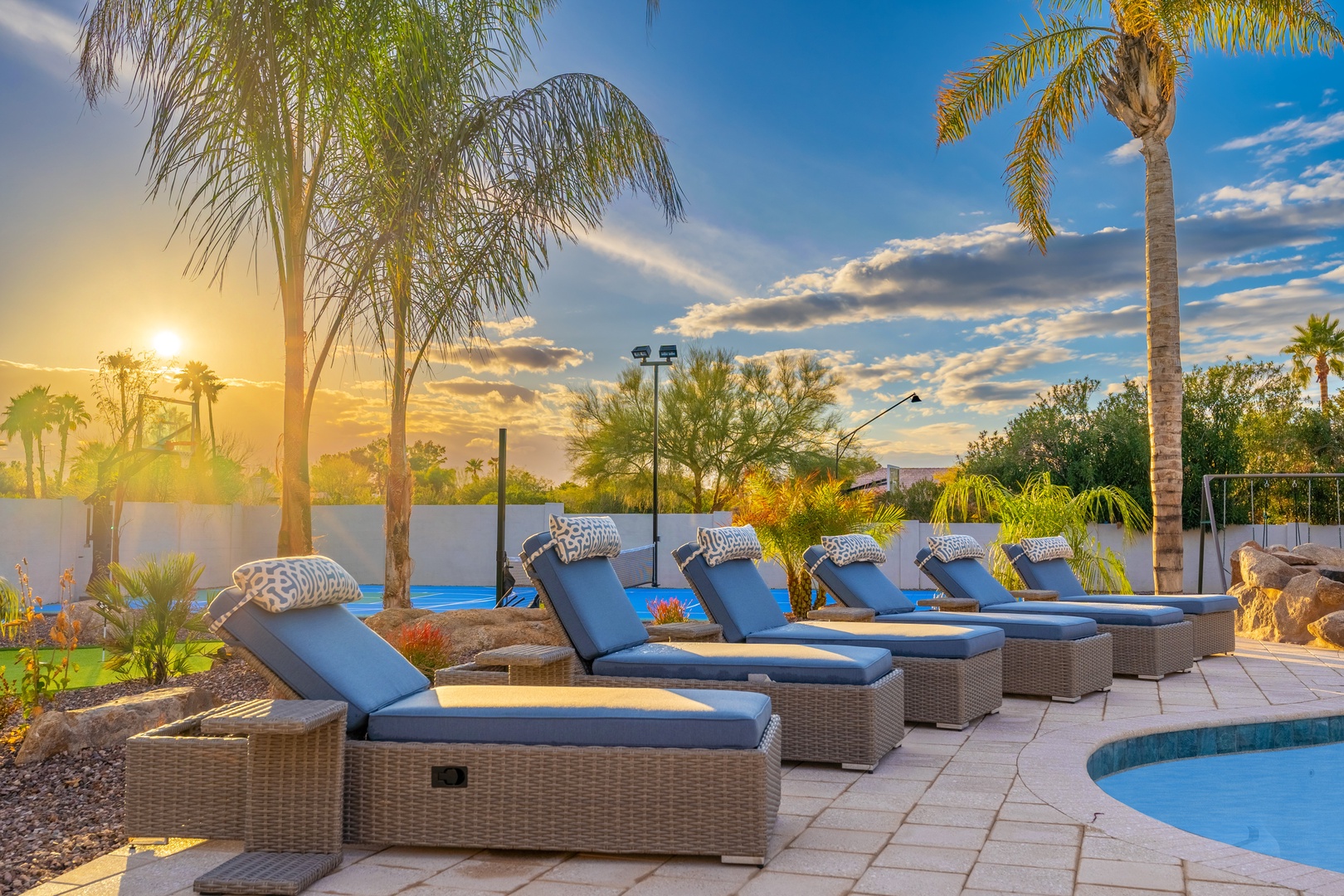 Golden hour light bathes the poolside lounge area, where palm trees sway against a dramatic desert sky—an inviting backdrop to the surrounding landscape.
