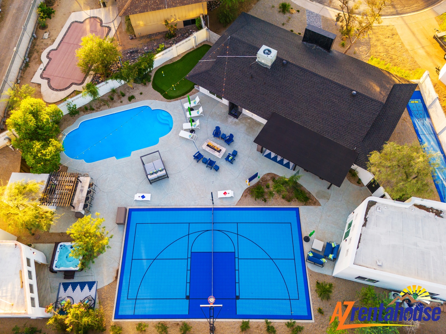 Aerial view of a spacious vacation rental property featuring a regulation basketball court, swimming pool, outdoor seating areas, and lush landscaping in a quiet residential neighborhood.