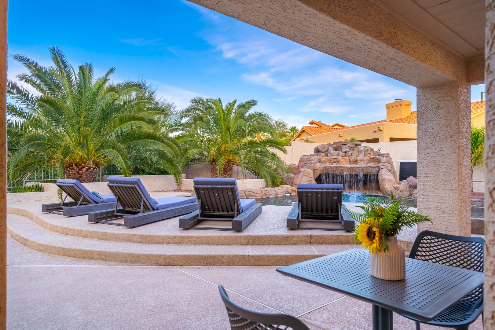 Lounge by your private pool and waterfall feature, soaking in desert sunshine from the comfort of your shaded patio with lush palm trees framing the view.