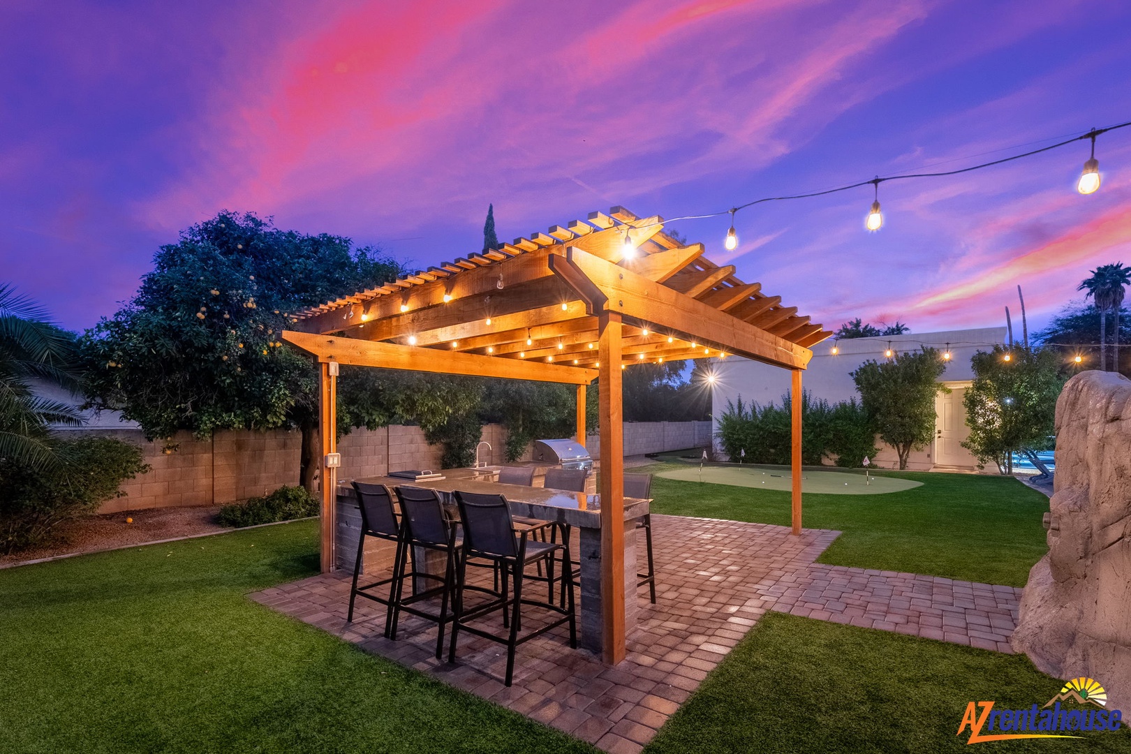 Stunning desert backyard features pergola dining, string lights, and pristine landscaping under dramatic purple sunset skies.