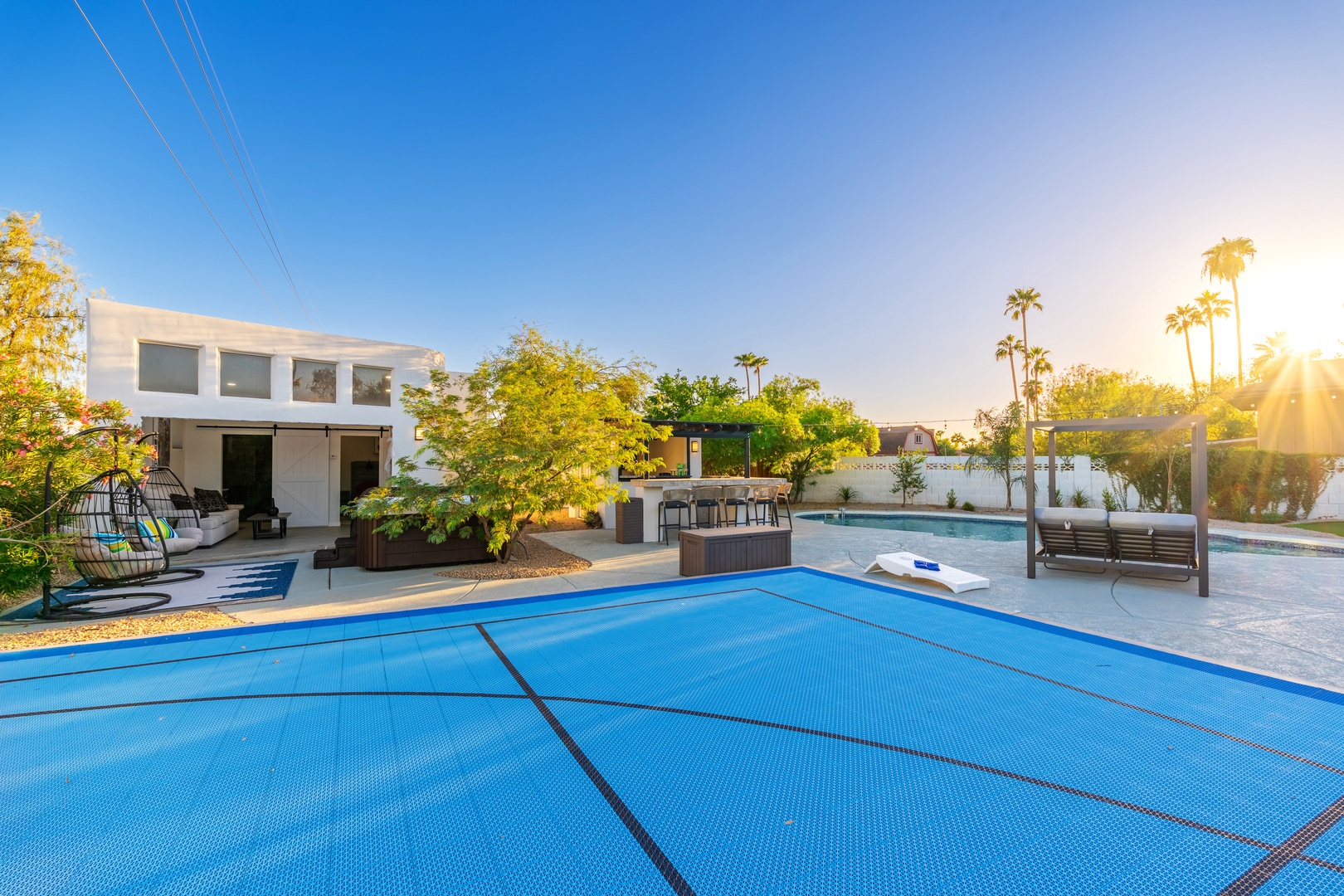 Expansive backyard with covered pool, spa, outdoor kitchen, and lush greenery under palm trees—perfect for entertaining or unwinding under the desert sun.