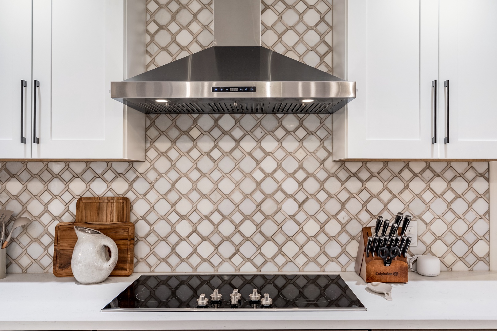 Cook your favorite meals on a sleek gas cooktop beneath a stylish stainless-steel range hood. Bright white cabinetry and elegant patterned backsplash make this kitchen ready for your culinary adventures.
