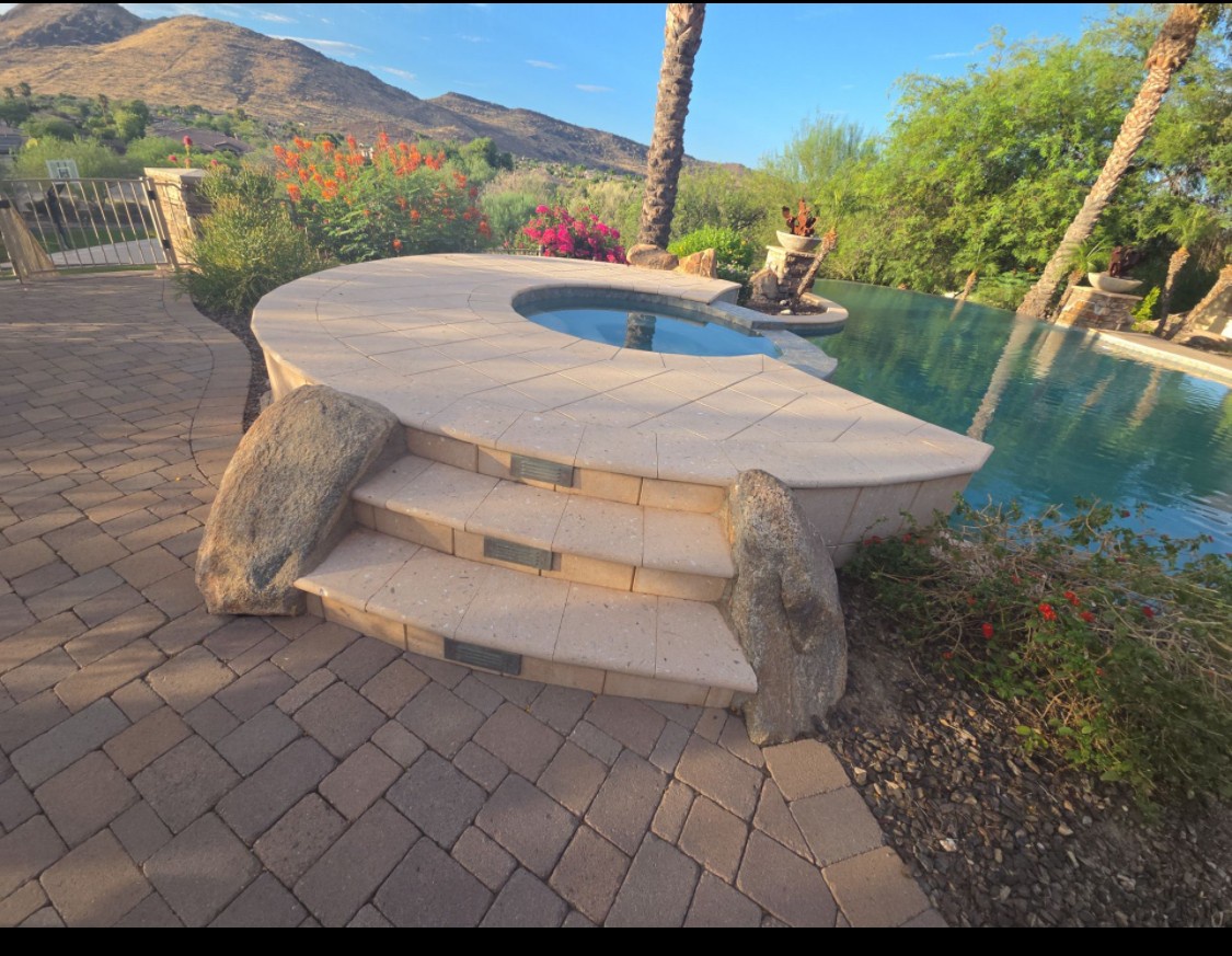 A stunning infinity pool framed by desert palms and mountain vistas, featuring an elegant stone entry with natural rock accents surrounded by vibrant desert blooms.