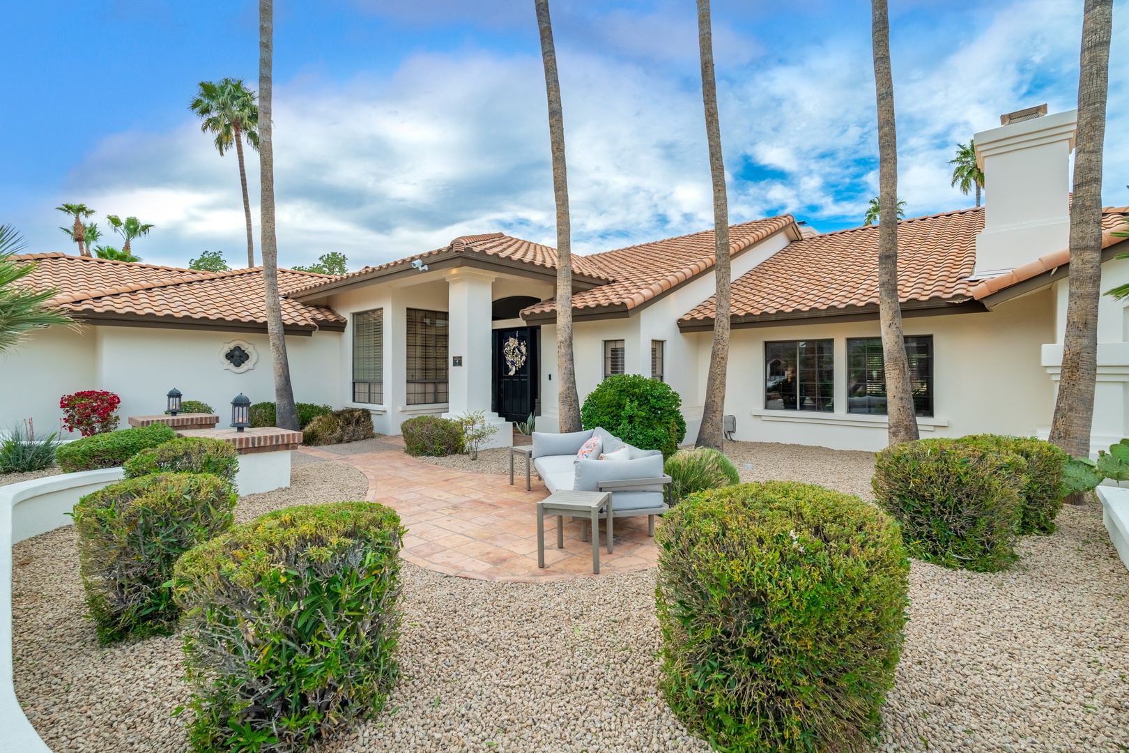 Mediterranean-style rental framed by stately palms and manicured gardens, blending desert elegance with comfortable outdoor seating perfect for arrival moments and sunset skies overhead.
