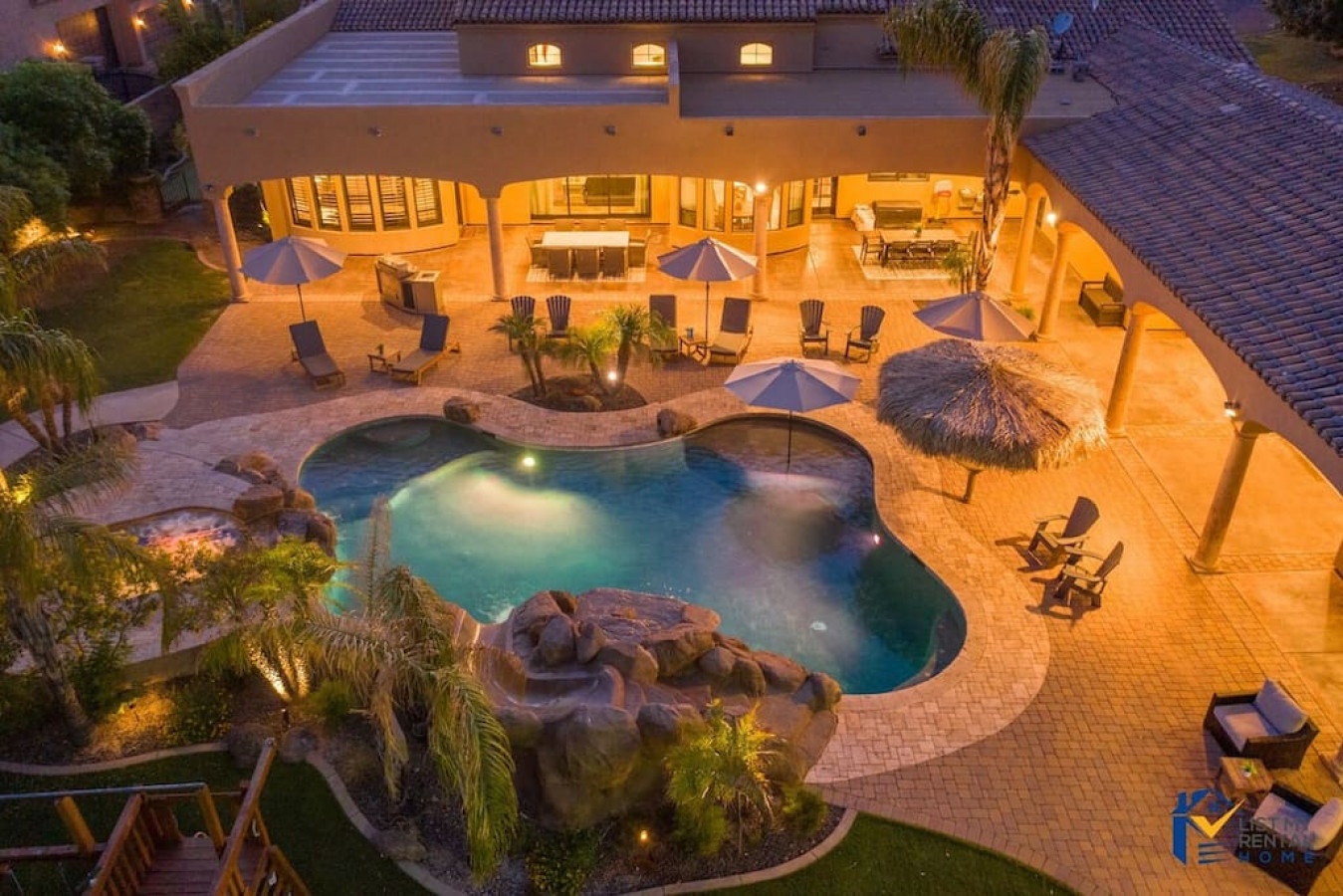 Aerial evening view of luxury villa with custom pool, spa, outdoor dining, and expansive entertaining spaces illuminated for nighttime ambiance.