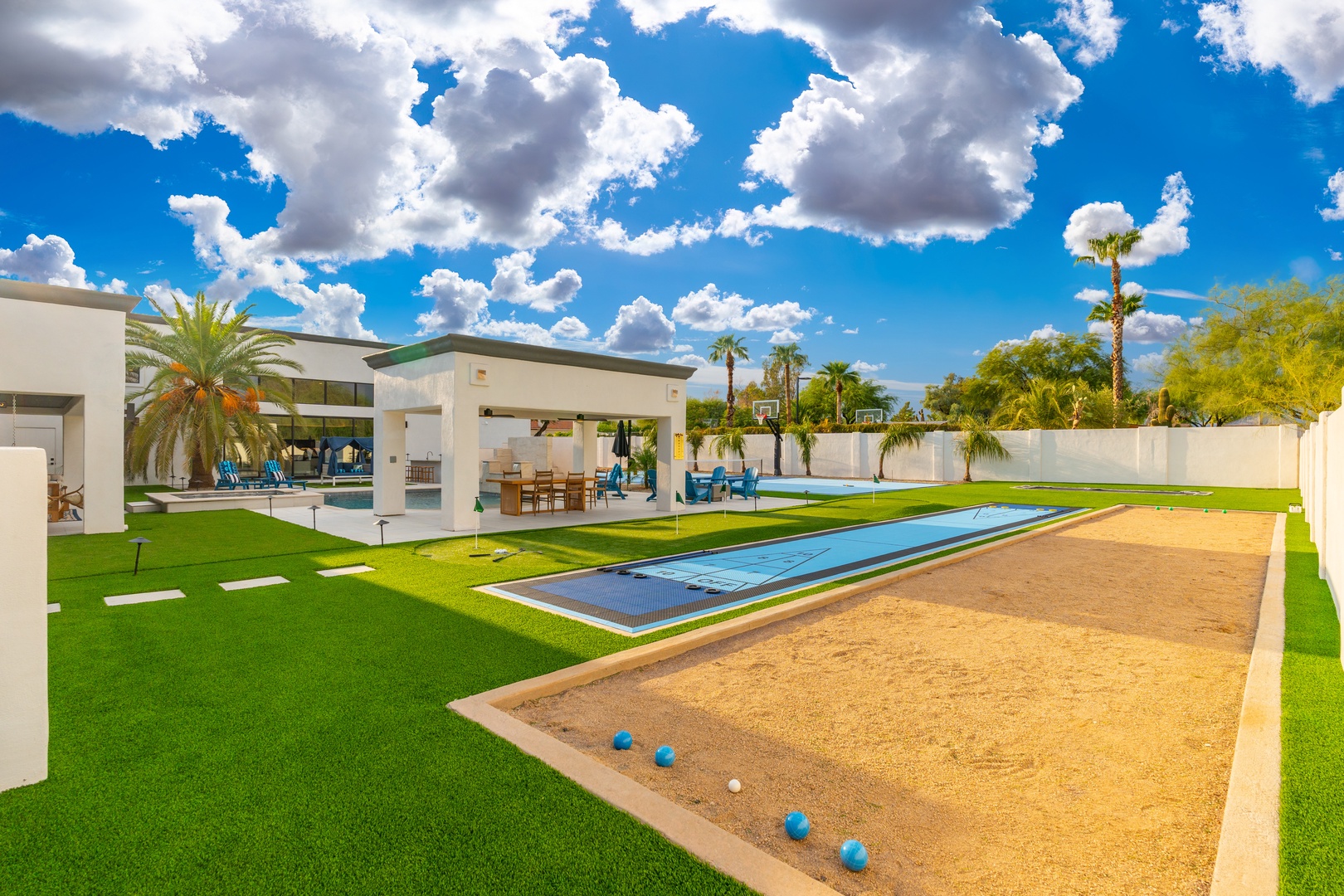A modern desert oasis with expansive lawn, sparkling pool, and shaded outdoor pavilion beneath dramatic skies—framed by palm trees and mountains.