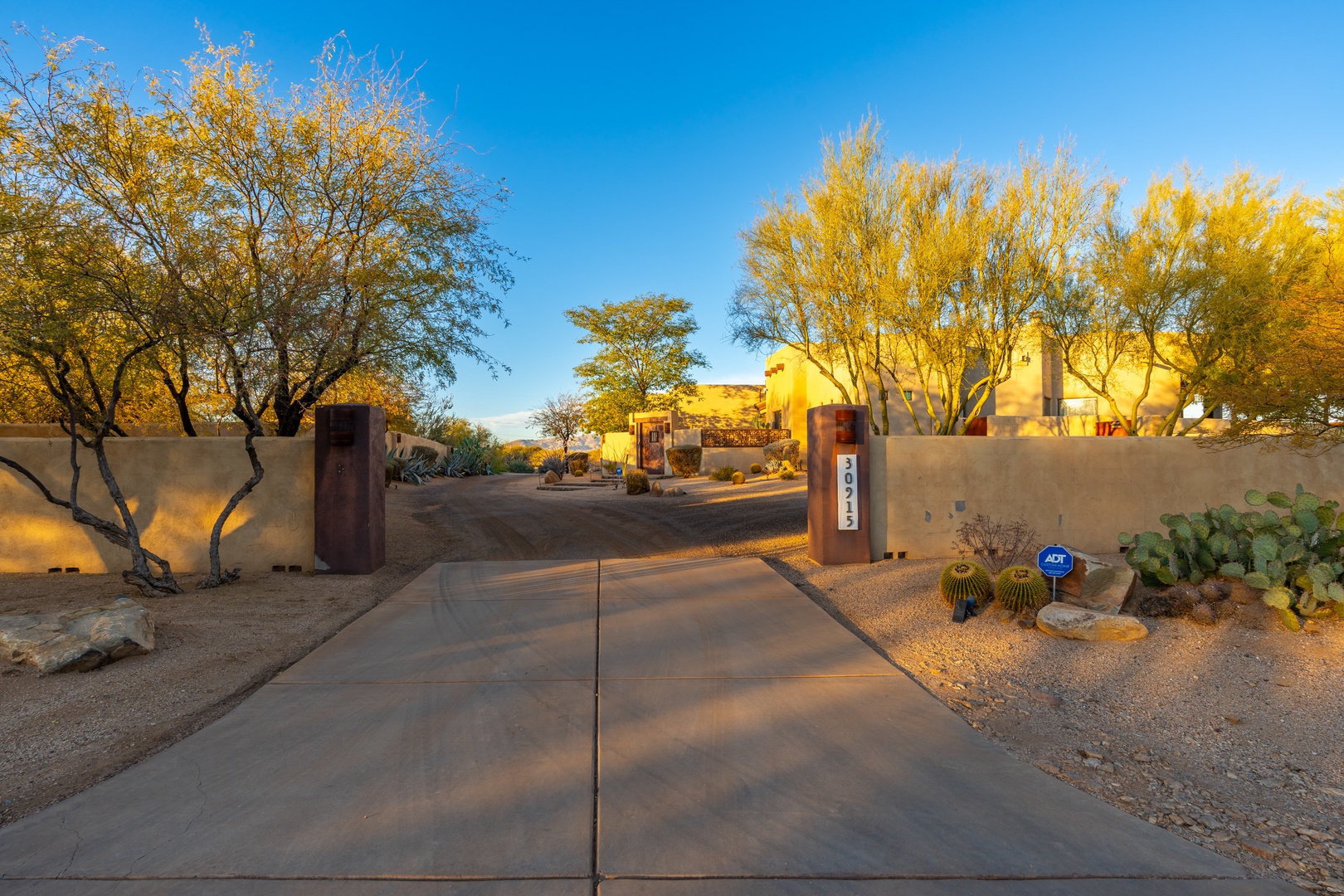 A welcoming entrance with desert landscaping and golden autumn trees frames the property's southwestern-style exterior, with address markers guiding your arrival to this peaceful retreat.