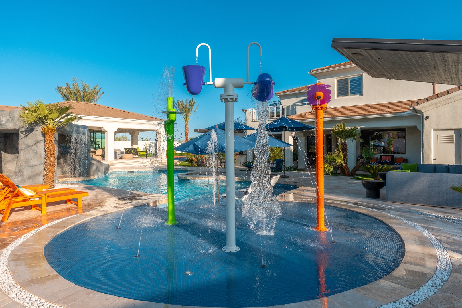 A vibrant splash pad with colorful water features provides endless fun for the little ones under clear desert skies, with lounge chairs and the main house steps away.