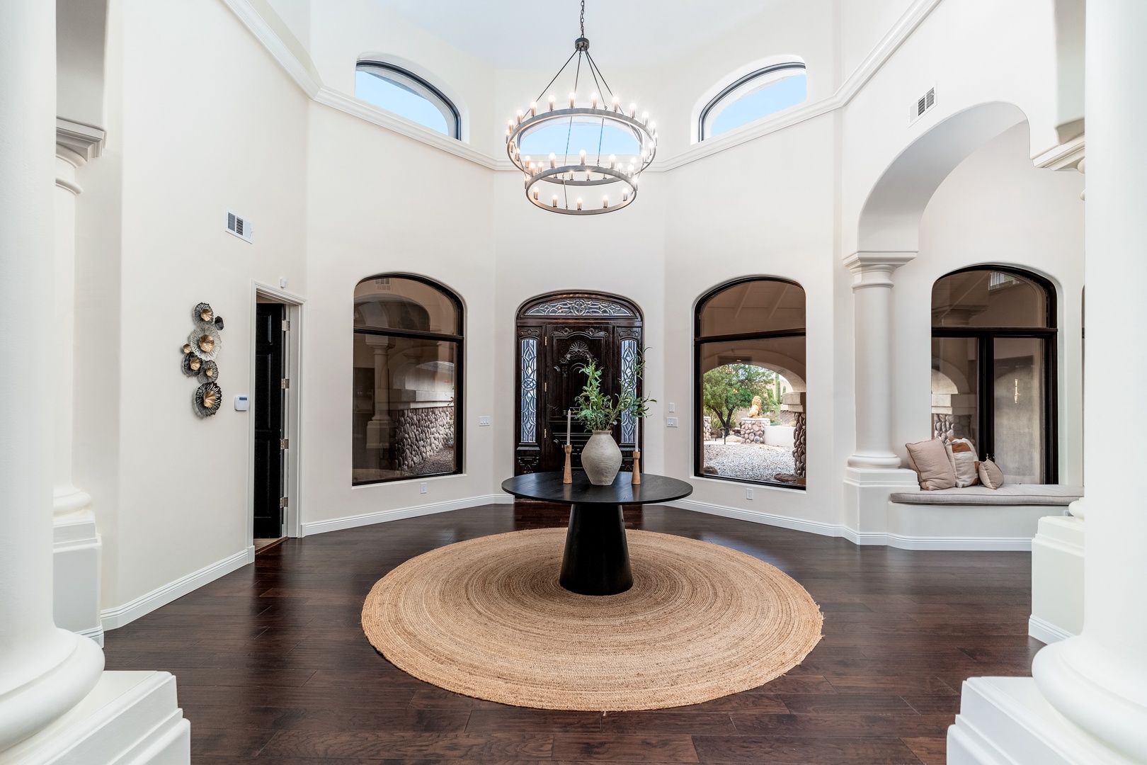 Step into an elegant foyer where soaring ceilings and graceful arches welcome you home. Natural light pours through arched windows, illuminating rich wood floors and creating a warm, inviting atmosphere for your arrival.