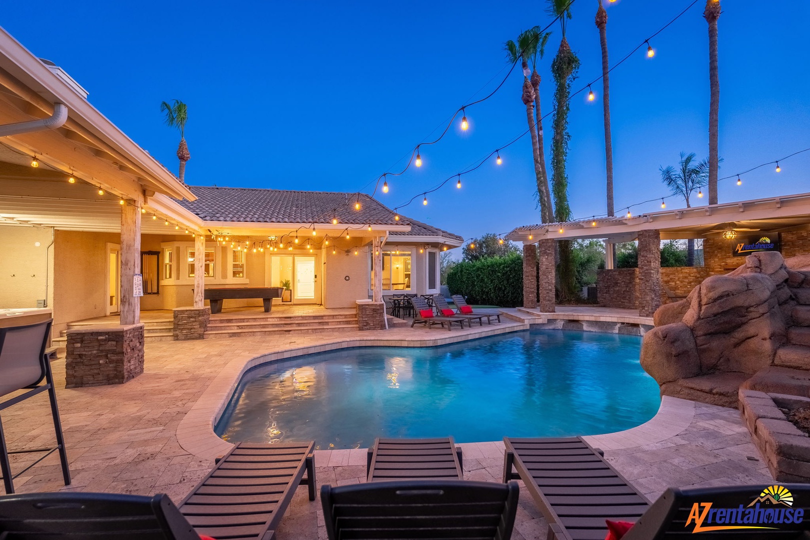 A stunning desert oasis awaits with a sparkling pool framed by palm trees and festive string lights, perfect for twilight relaxation under Arizona skies.