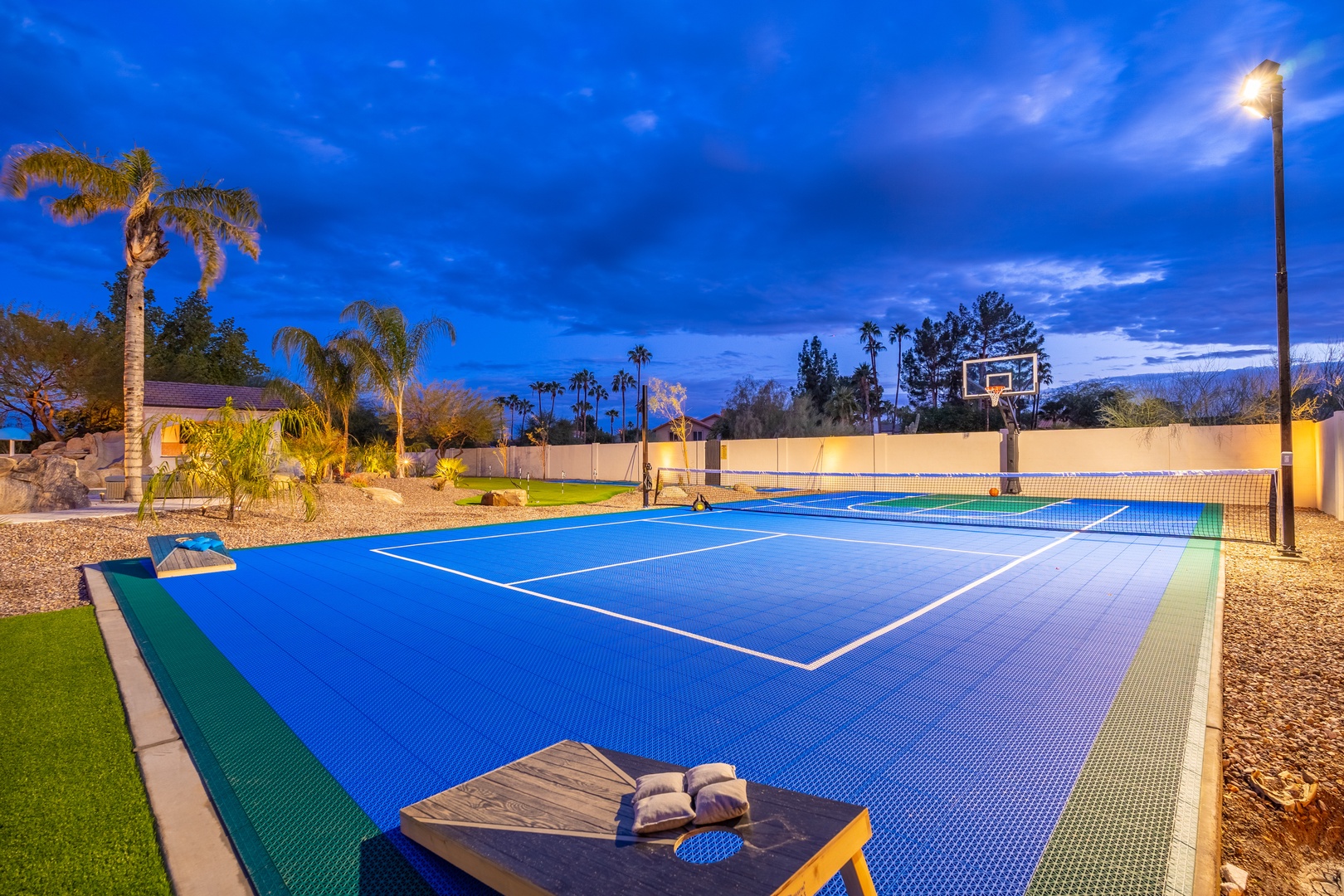 A multi-sport recreation area featuring tennis and pickleball courts under evening lighting, surrounded by tropical landscaping and lush green spaces.