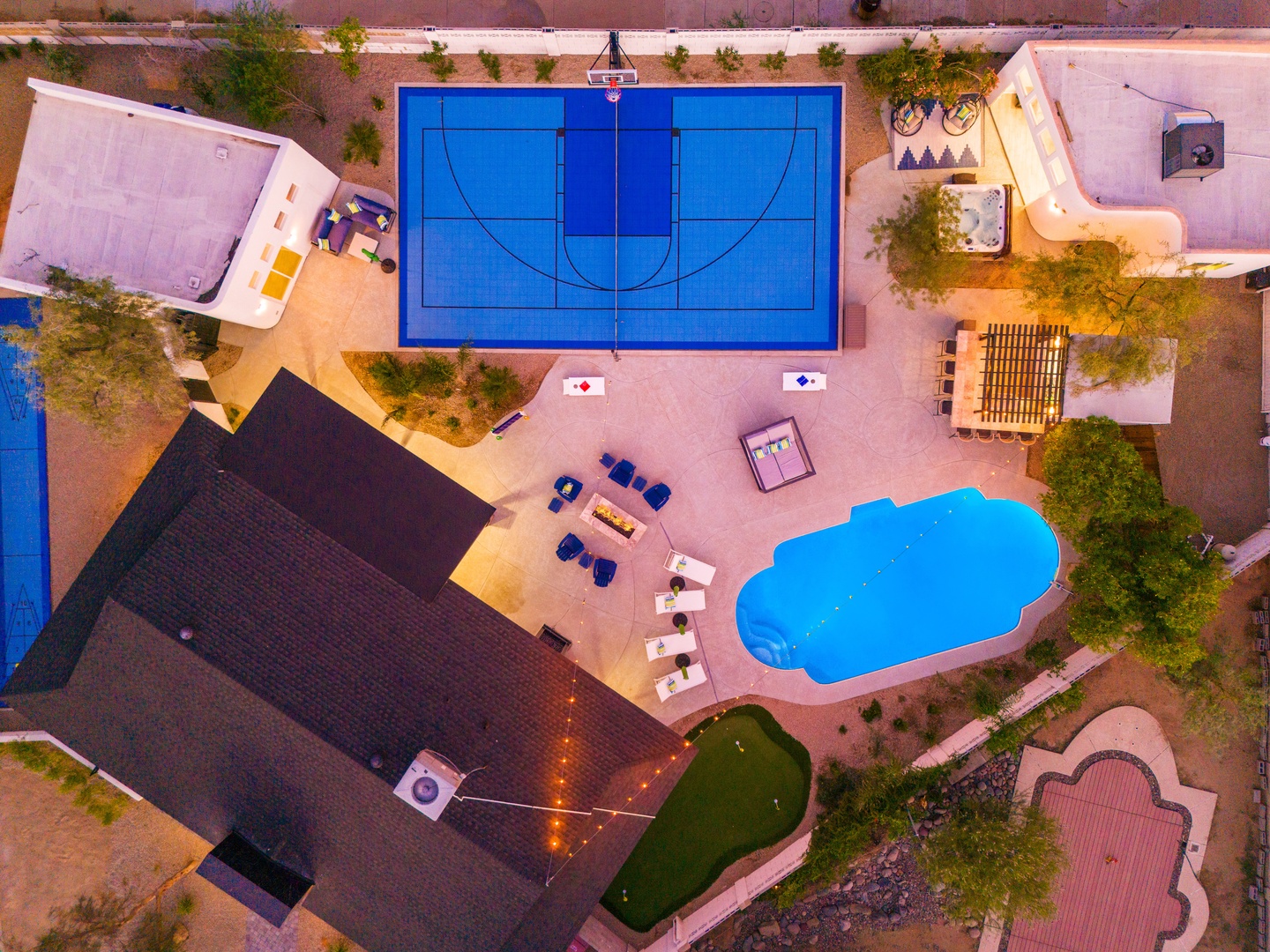 Aerial view of a desert vacation retreat featuring a full-size basketball court, private pool with poolside seating, and multiple outdoor recreation areas surrounded by natural landscaping.