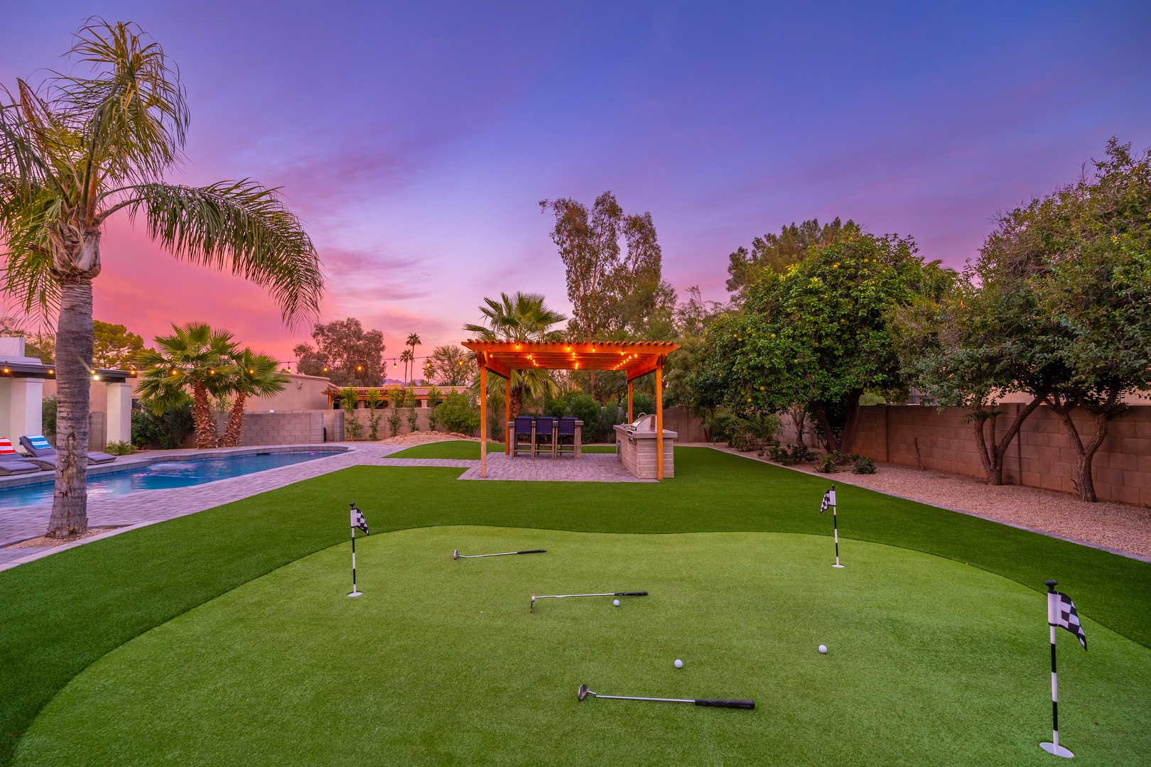 A private putting green, sparkling pool, and shaded pergola await beneath stunning desert sunset skies—an entertainer's dream backyard oasis.