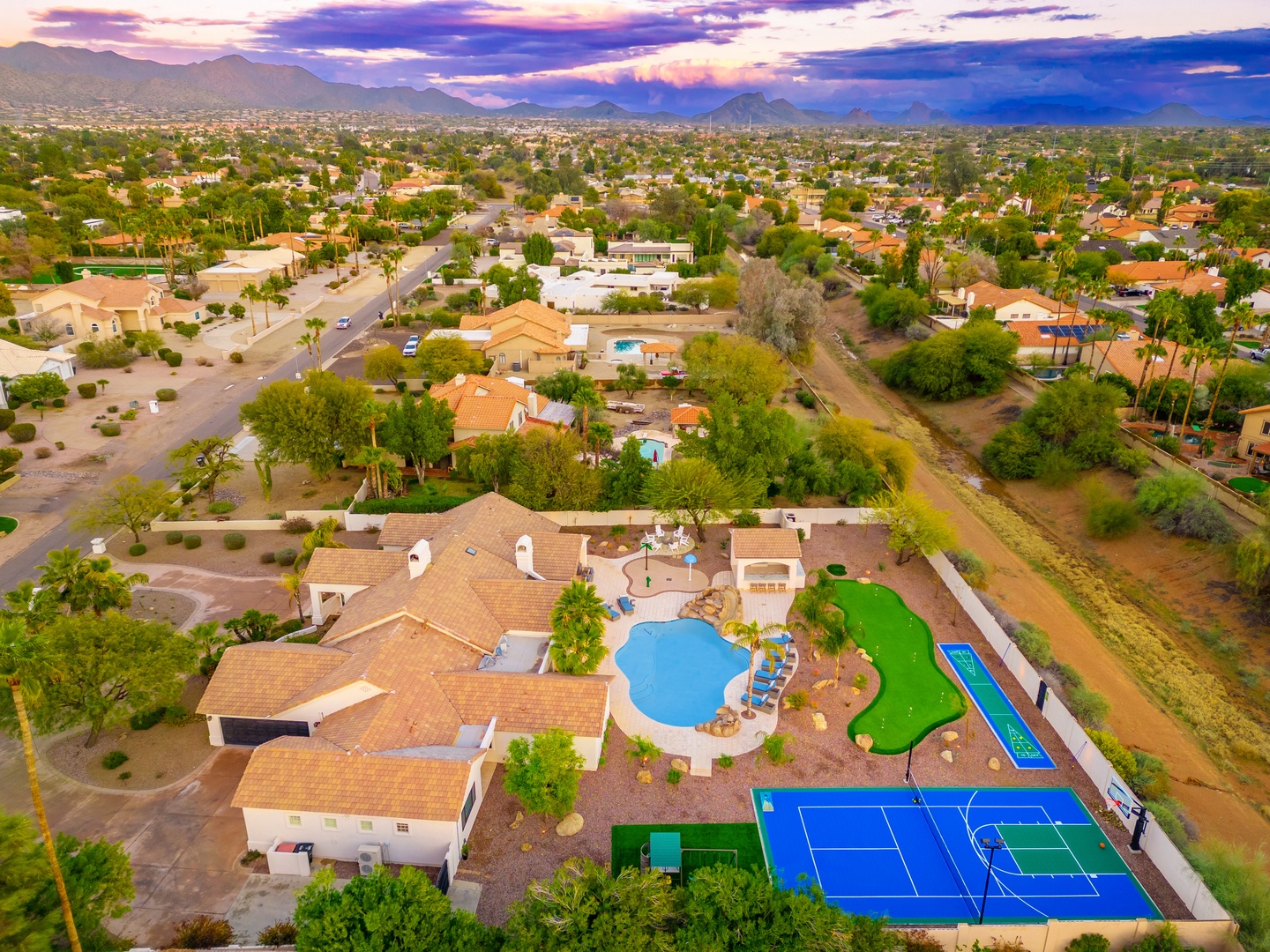Aerial view showcasing the expansive property with pool, tennis court, and mountain backdrop in a serene desert neighborhood.