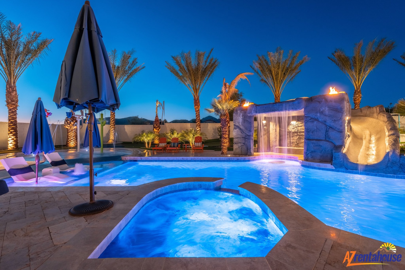 A stunning desert oasis awaits with crystal-clear pool, bubbling spa, and magical lighting beneath towering palms and starlit skies.