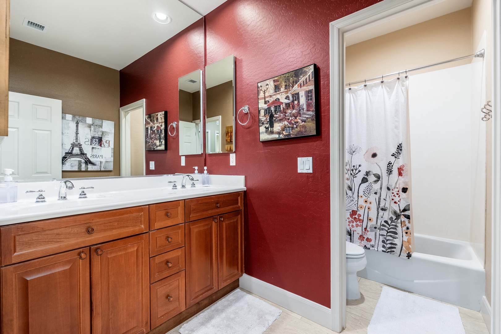 Step into your private bathroom—a stylish retreat featuring warm wood cabinetry, elegant dual sinks, and a deep tub behind a charming floral curtain, perfect for unwinding after exploring.