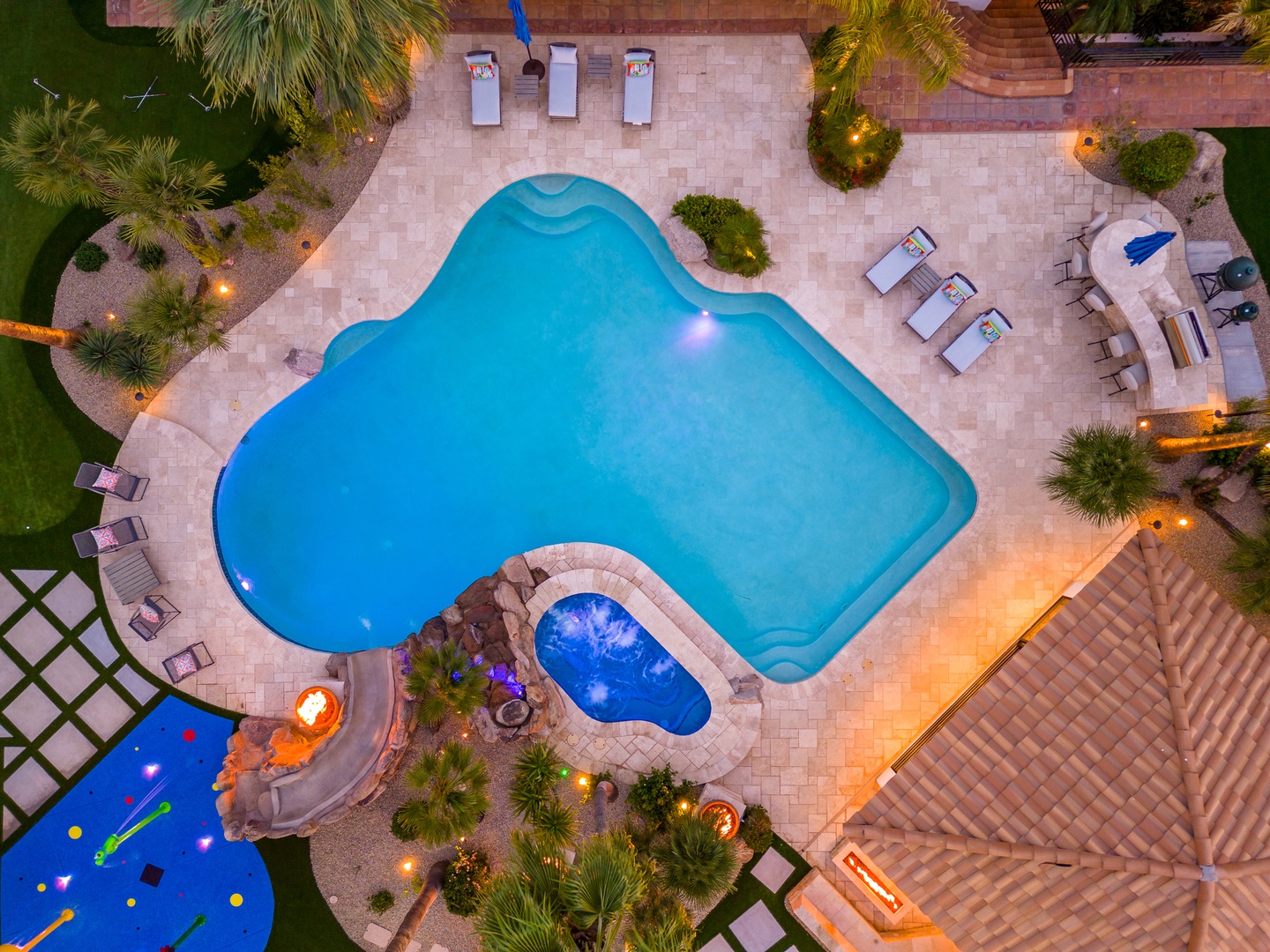 An aerial view captures the property's inviting pool complex at dusk, with tropical landscaping, a hot tub, outdoor seating areas, and warm lighting creating a resort-like ambiance.