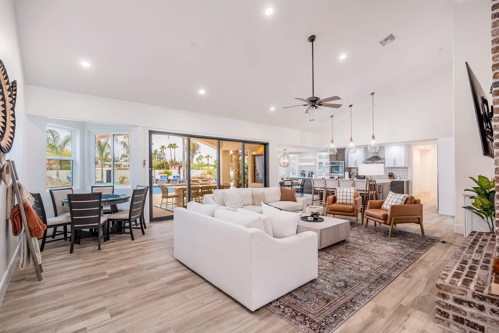 Unwind in your spacious open-concept living area where natural light floods through floor-to-ceiling glass doors, revealing pool views and palm trees beyond your comfortable retreat.