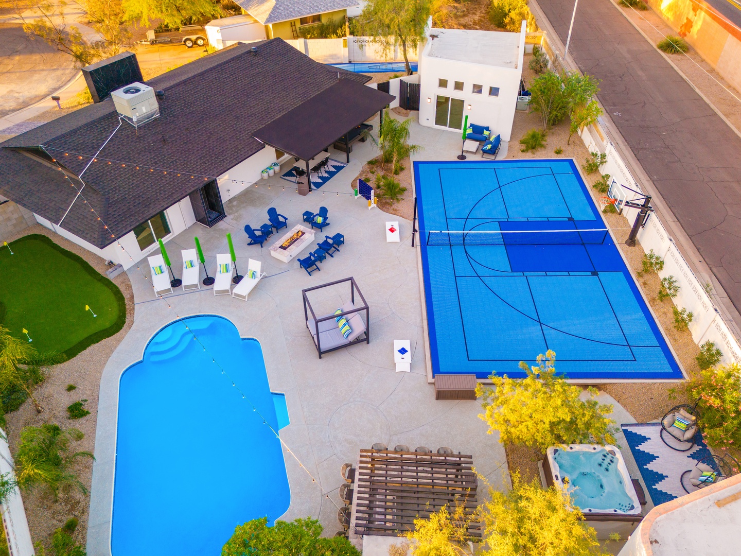 Aerial view reveals the property's extensive outdoor entertainment area, featuring a custom-shaped pool, regulation sport court, hot tub, putting green, and covered patio seating.