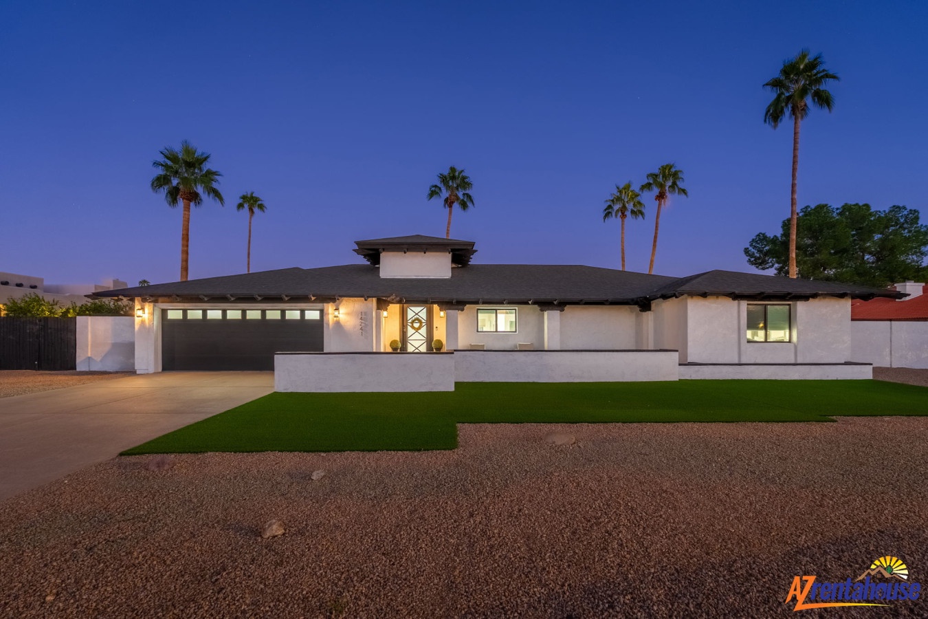 Modern ranch-style property featuring desert landscaping and palm trees under twilight skies.