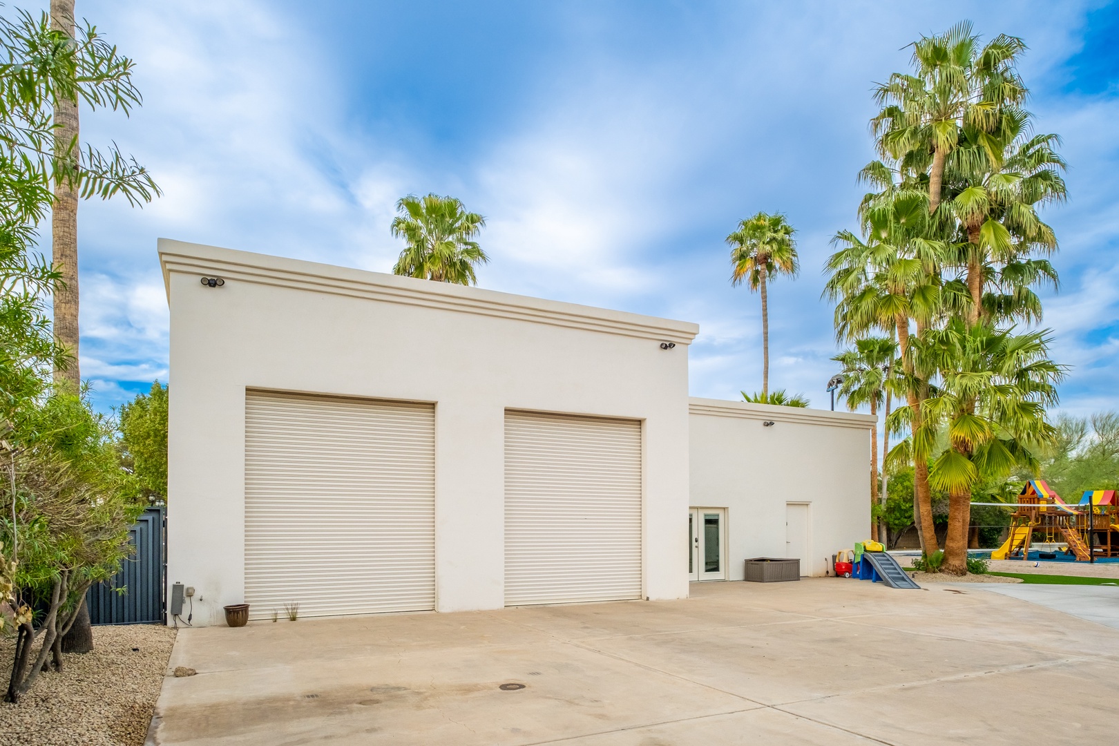 This contemporary desert property features a spacious two-bay garage with convenient roll-up doors, set amid mature palm trees and desert landscaping.