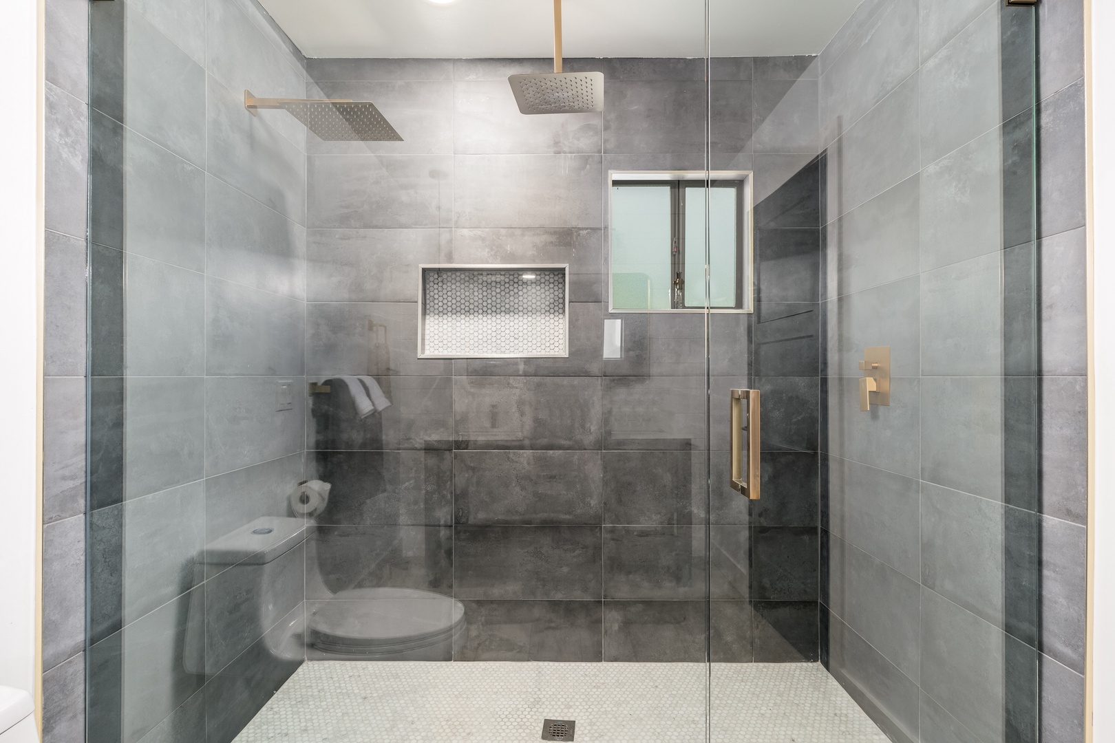 Step into your private spa retreat with dual rain showerheads, sleek gray tiling, and a built-in bench—perfect for unwinding after exploring.