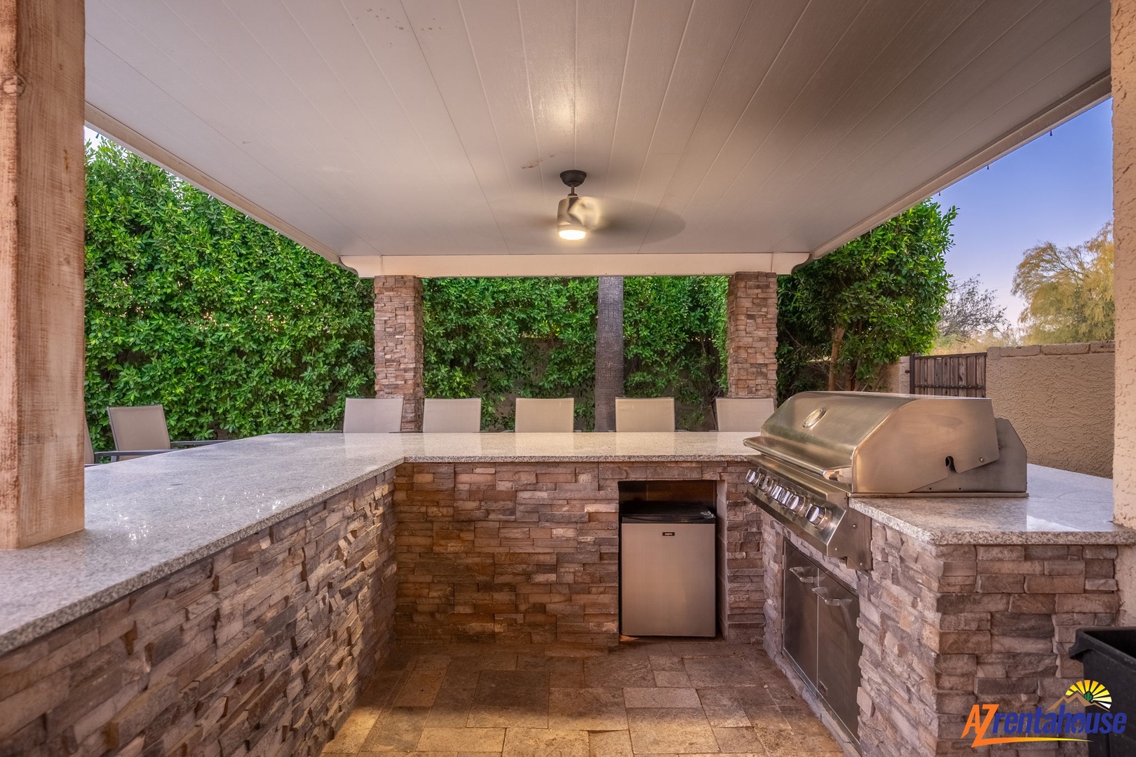 A covered outdoor kitchen with built-in grill and stone countertops, perfect for your memorable cookouts surrounded by lush greenery.