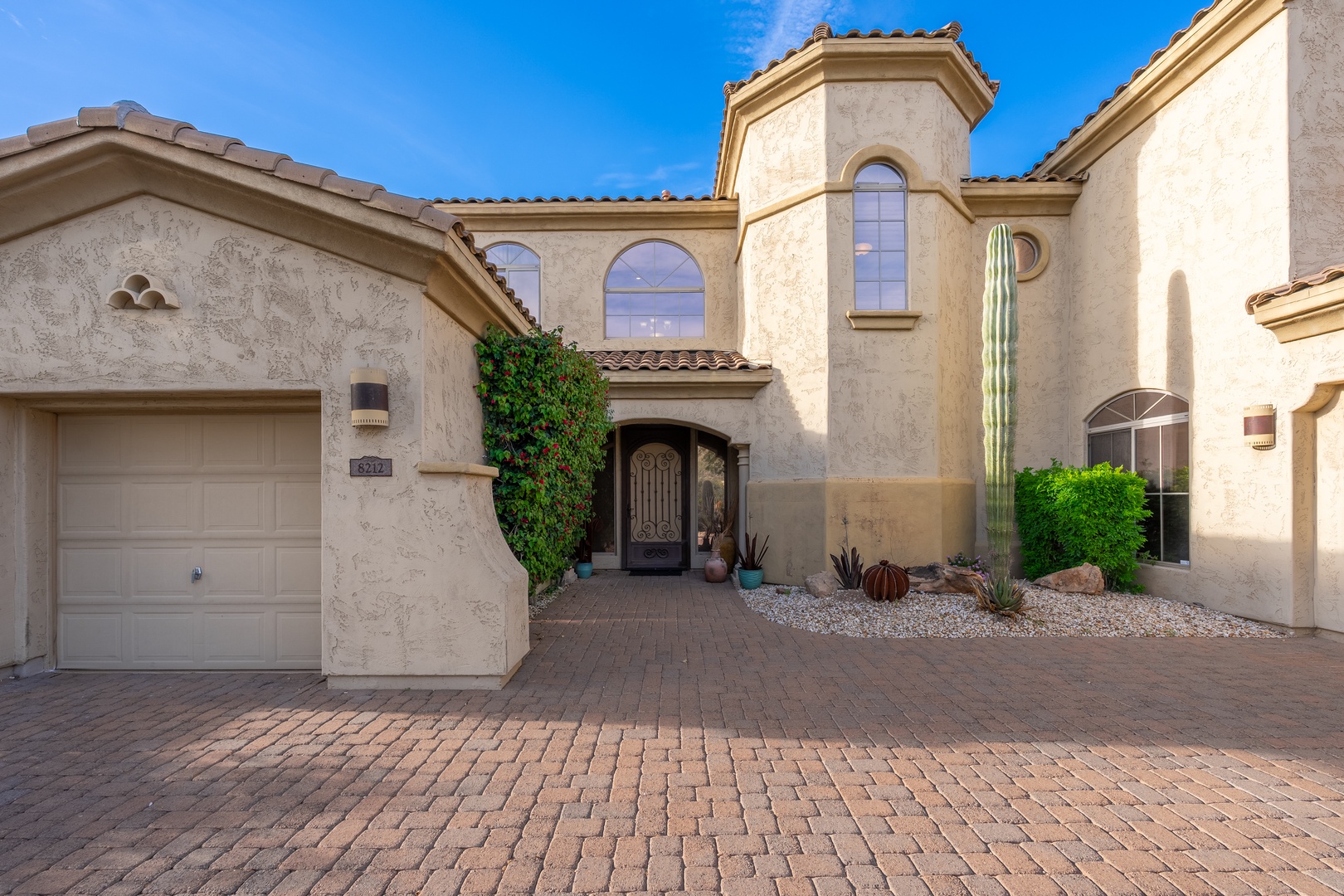 A striking Southwestern-style villa featuring elegant stucco walls, towering arched windows, and desert landscaping beneath a brilliant blue sky.