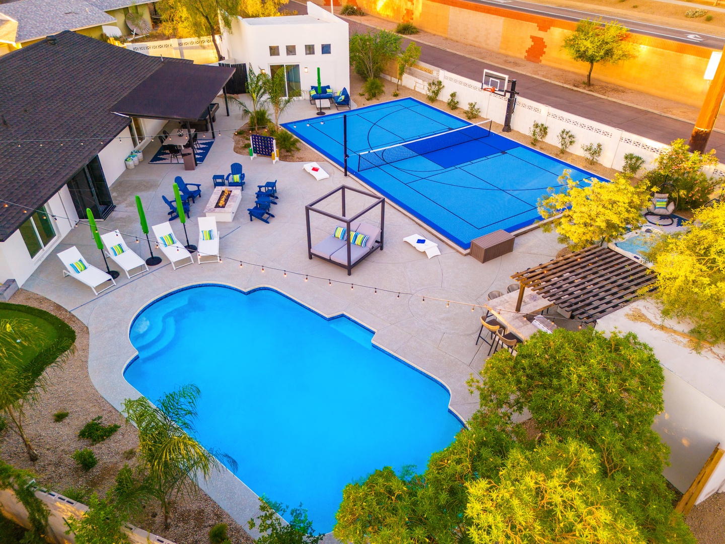 Aerial view of this property's extensive private outdoor amenities, featuring a spacious pool, sport court, covered patio, and landscaped grounds—all illuminated at dusk in a quiet residential neighborhood.