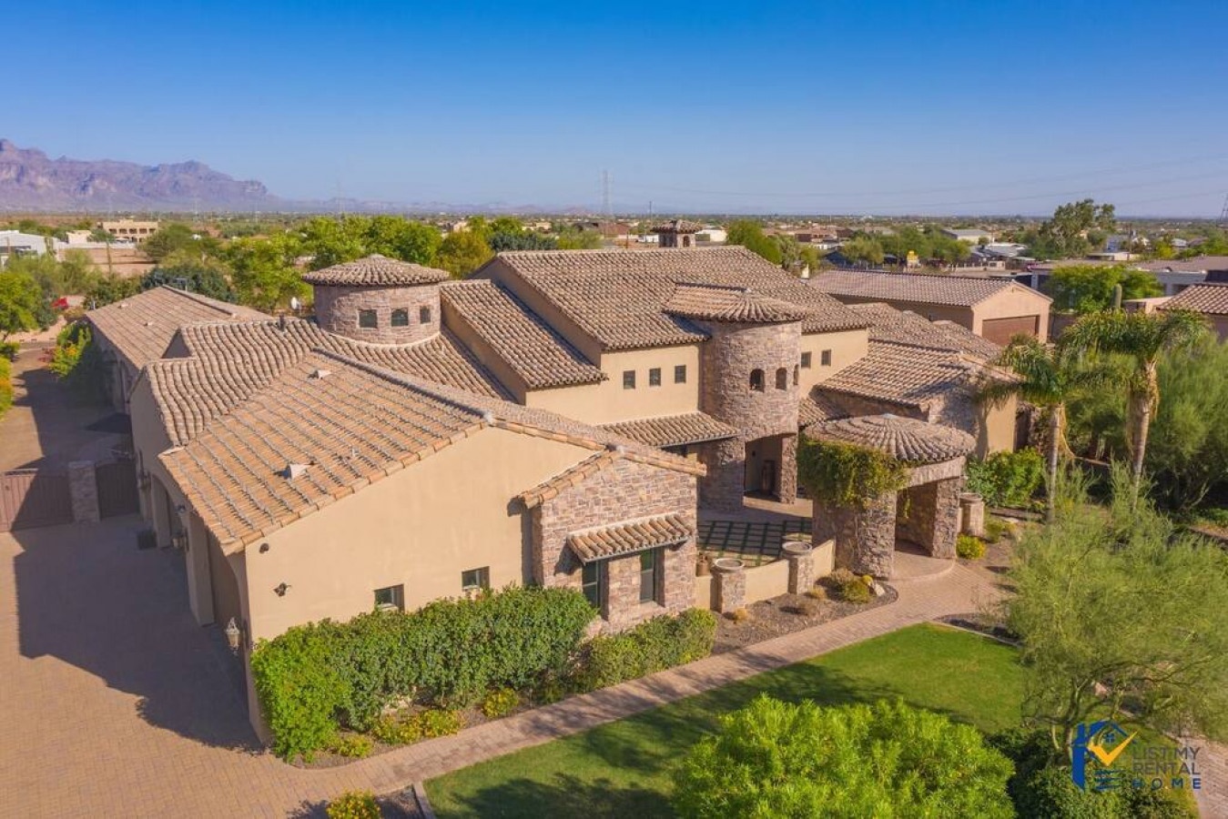 Sprawling desert villa with stone accents and tile roofing nestled in a quiet residential neighborhood with mountain backdrop.