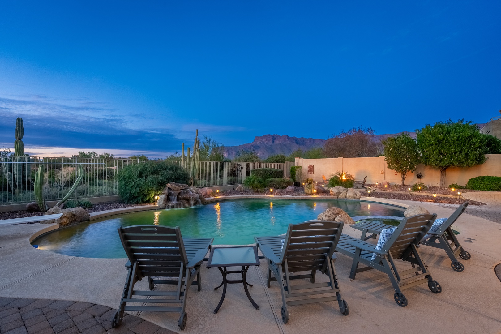 This stunning desert oasis features a sparkling pool surrounded by desert landscaping, dramatic mountain views, and comfortable poolside seating—perfect for your Arizona getaway as day transitions to night.