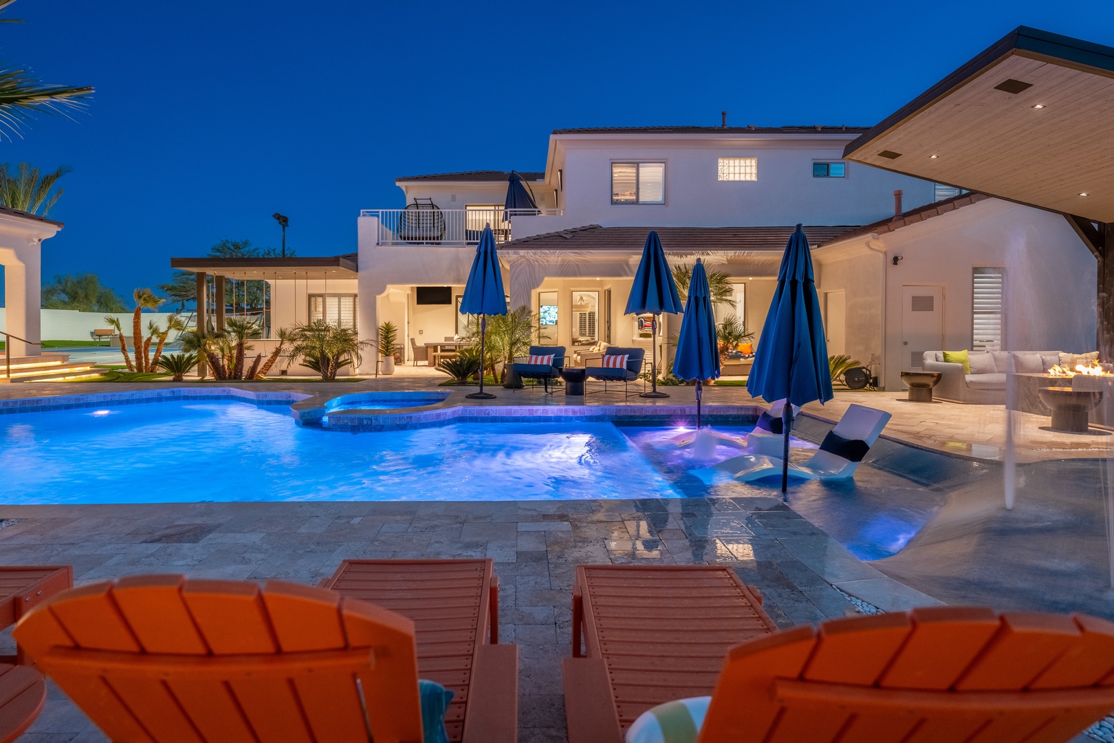 Modern luxury villa showcasing illuminated pool and spa with stylish lounge areas under a twilight sky—an elegant backdrop for the surrounding property.