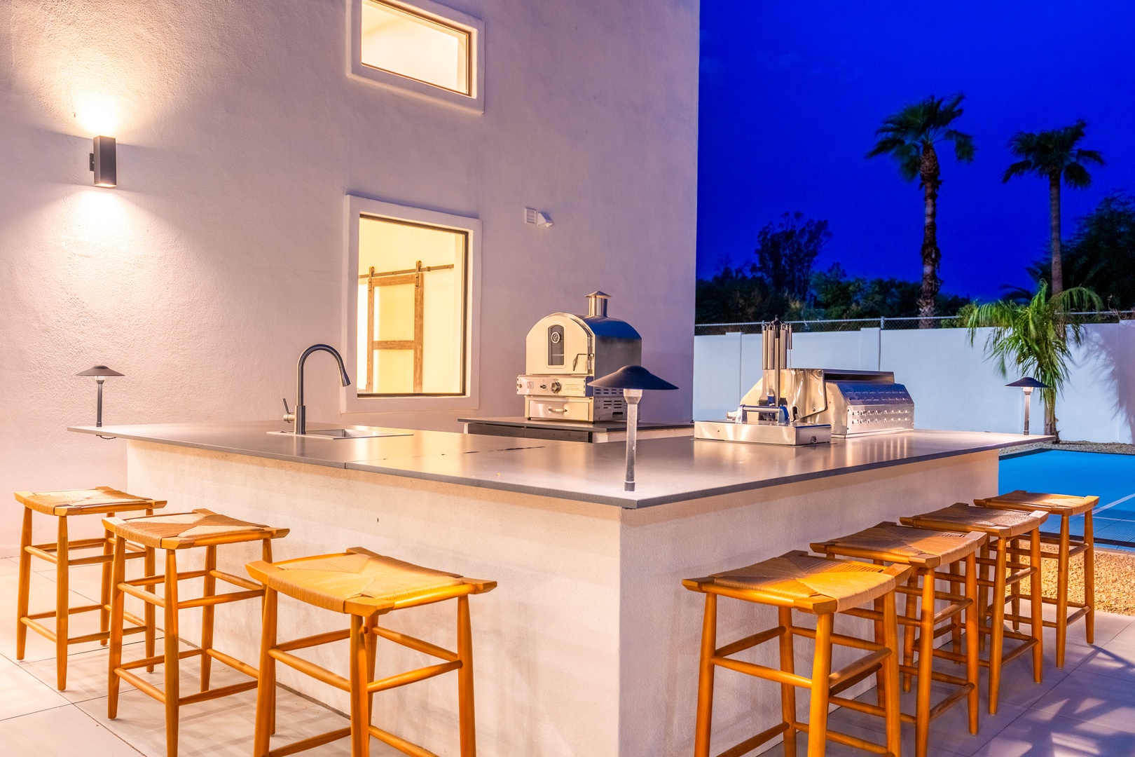 Your own outdoor kitchen awaits, complete with a sleek bar, pizza oven, and grill—perfect for evening meals under swaying palms and tropical skies.