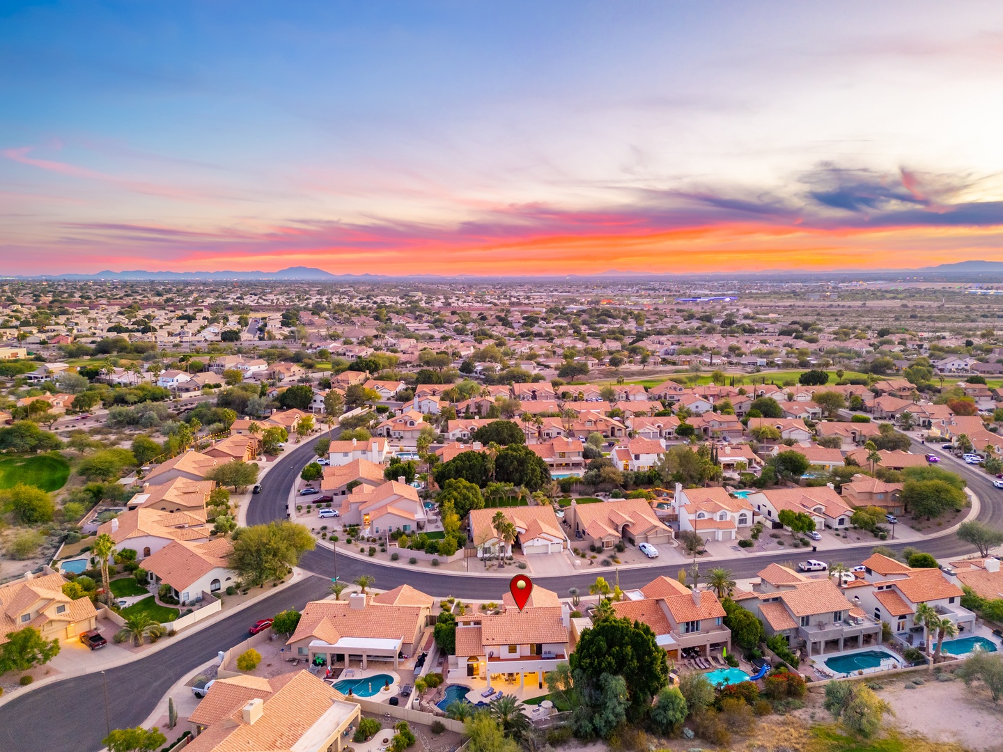 Aerial view of a residential neighborhood at sunset, showcasing the property's location within a peaceful desert community with mountain views on the horizon.