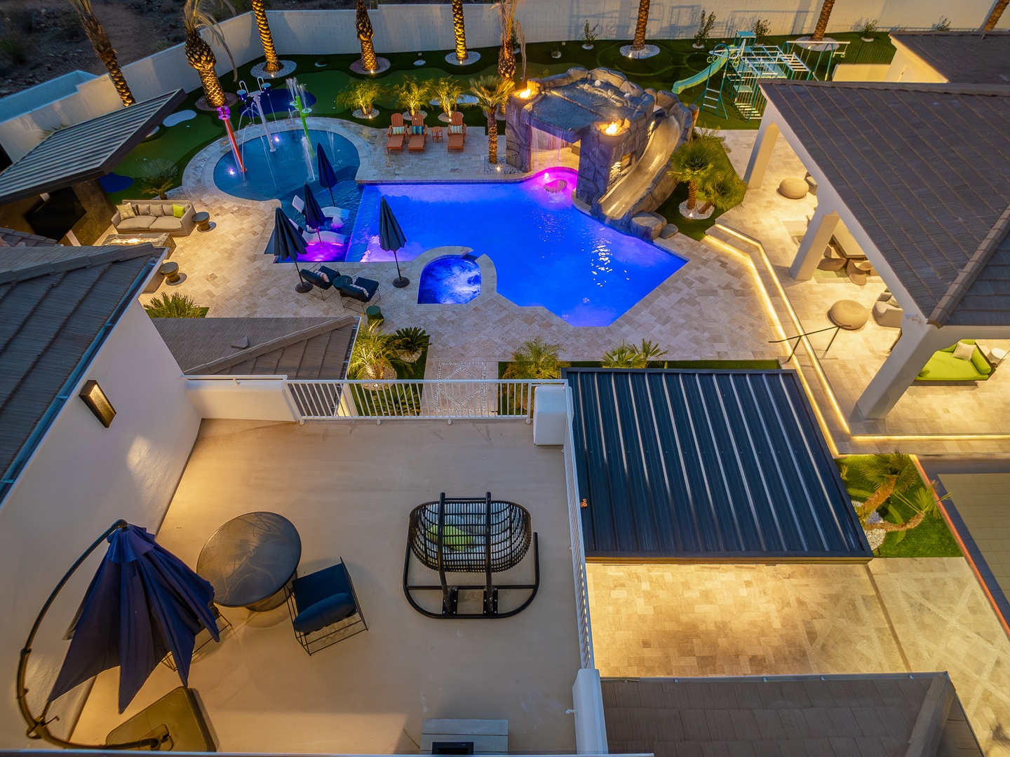 Aerial view captures the property's tropical resort-style backyard oasis featuring a custom pool with slide and spa, multiple outdoor lounging areas, palm trees, fire features, and modern covered patios perfect for entertaining.
