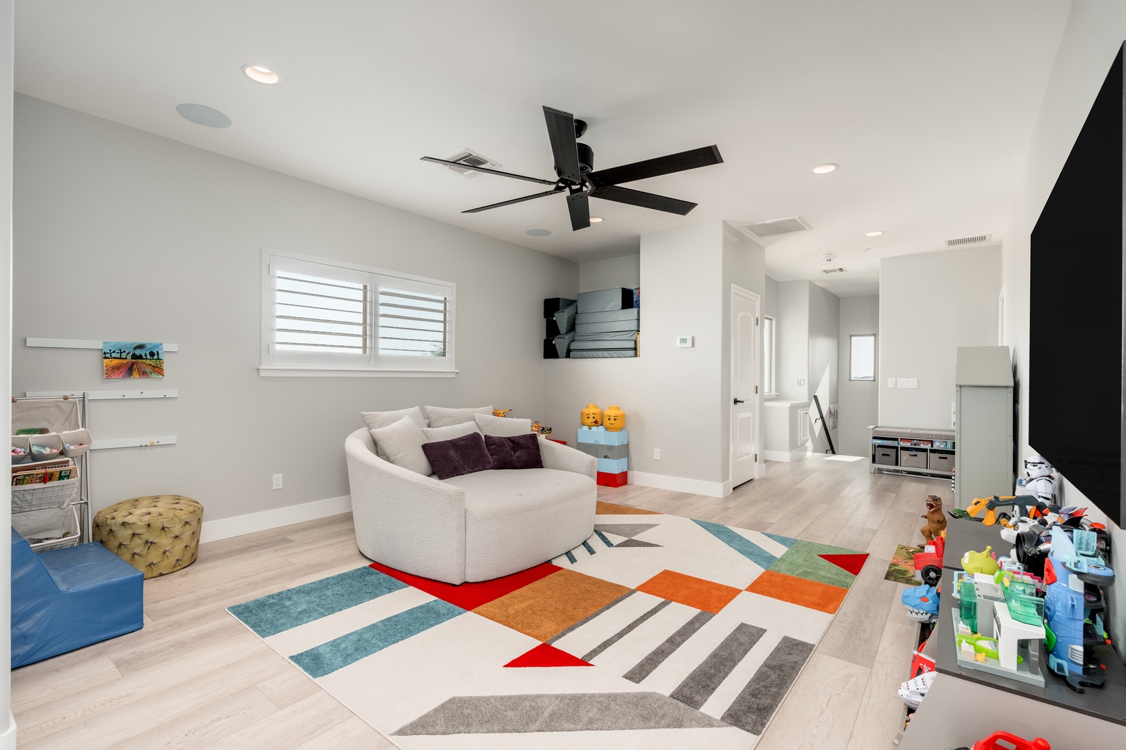 Sink into the curved sofa and enjoy family time in this bright, open play space. The colorful geometric rug and ceiling fan create a cheerful environment perfect for relaxation and fun.