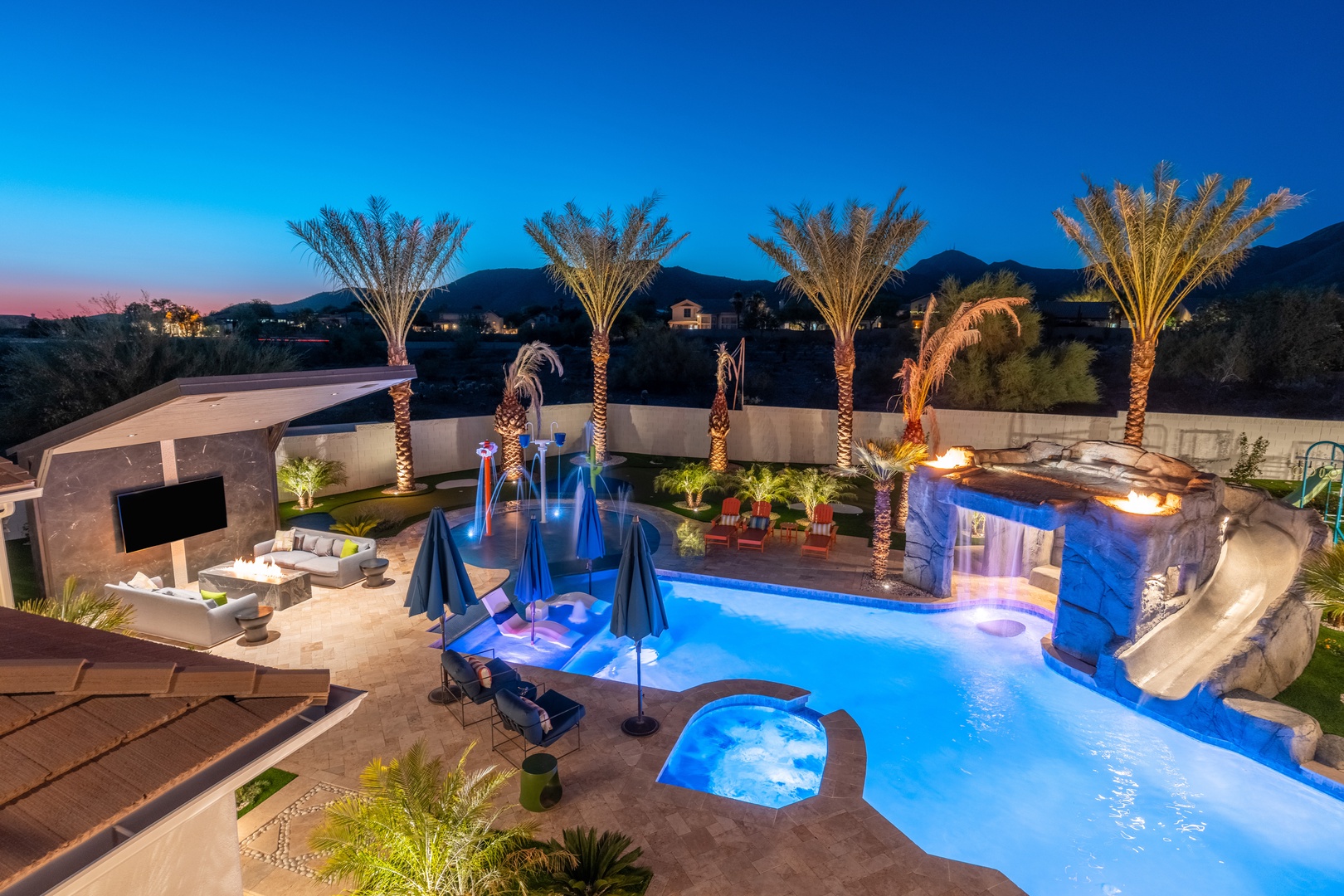 Stunning resort-style backyard retreat featuring a lagoon pool with waterslide, spa, fire features, and lush palm landscaping against mountain views at twilight.