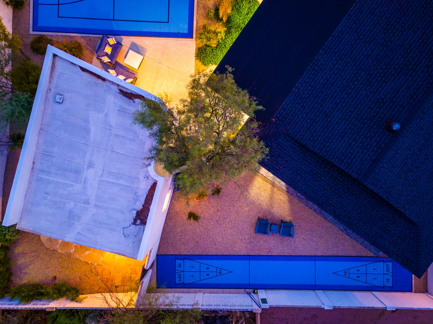 Aerial view showcasing the property's evening ambiance with illuminated swimming pool, outdoor seating areas, and landscaped grounds framed by warm accent lighting.