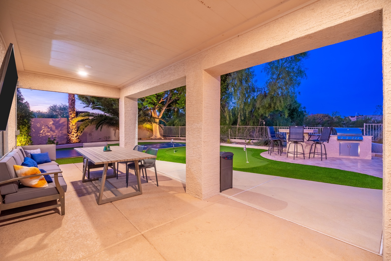 Your private covered patio opens to a resort-style backyard with a sparkling pool, lush green lawn, outdoor bar, and ambient lighting—perfect for evening relaxation under the stars.