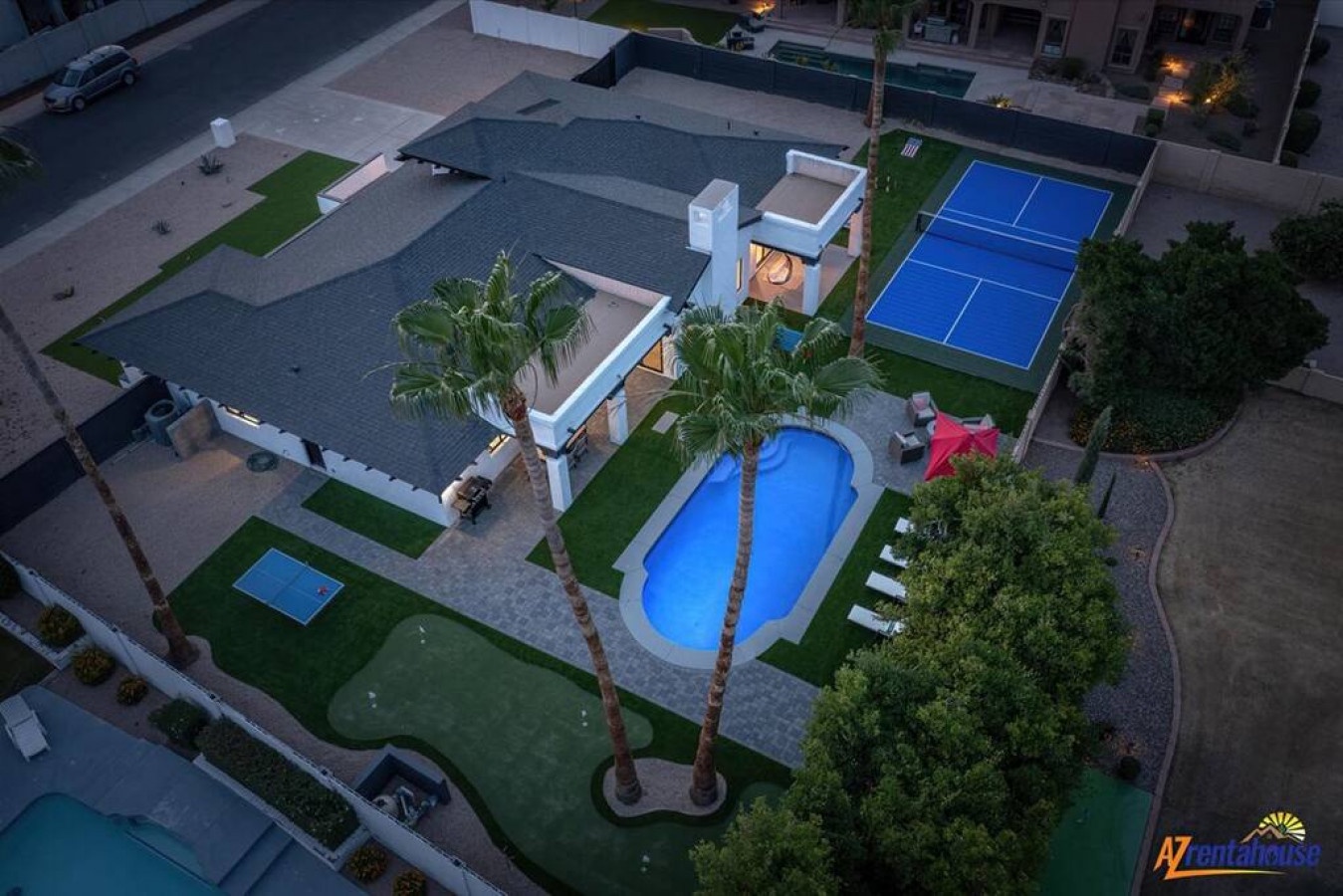 Aerial view of a luxury vacation rental featuring a sparkling pool, tennis court, and manicured gardens in a quiet residential neighborhood.