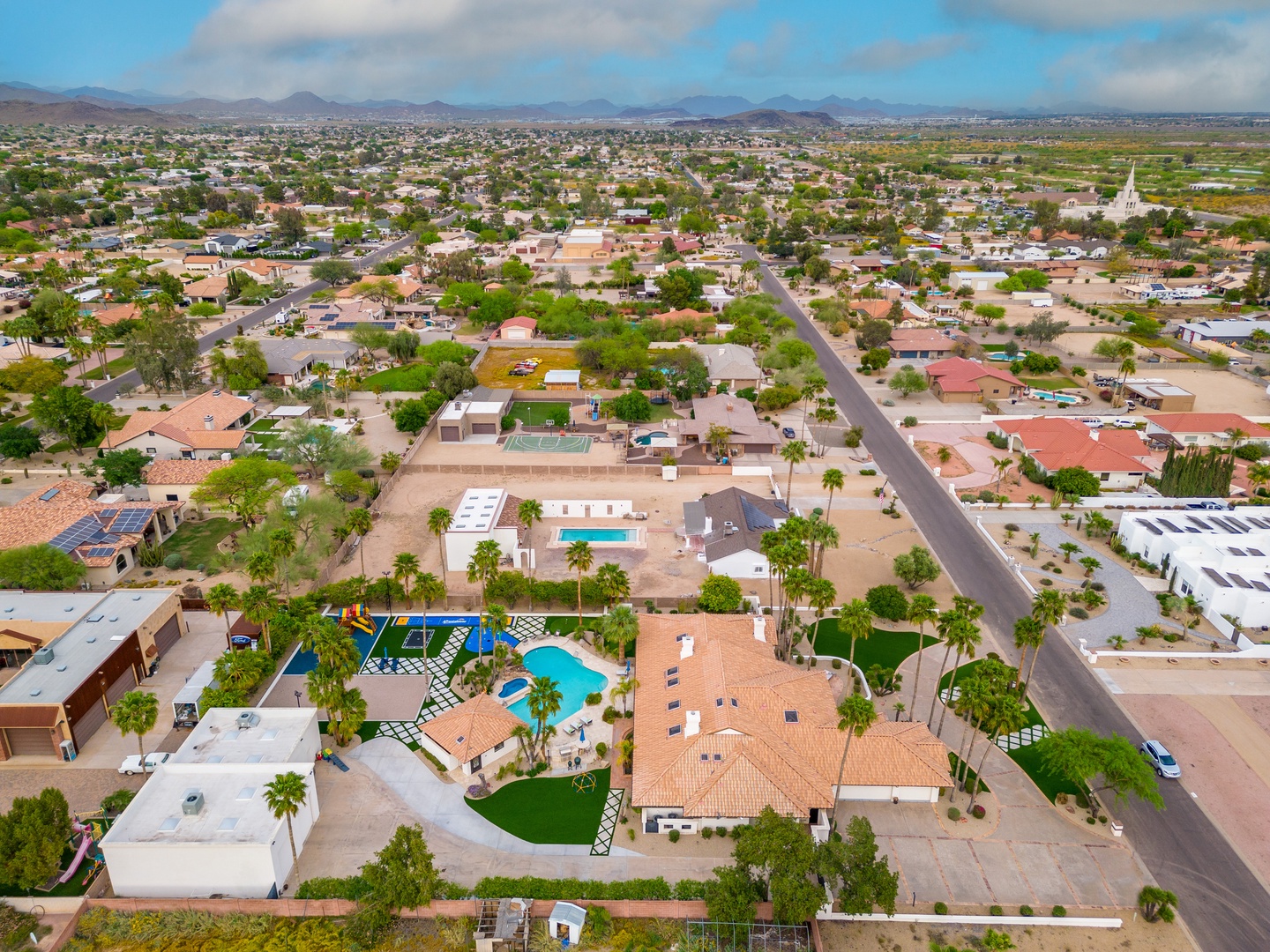 Aerial view of a residential neighborhood showcasing the property's location among palm-lined streets and desert mountain vistas.