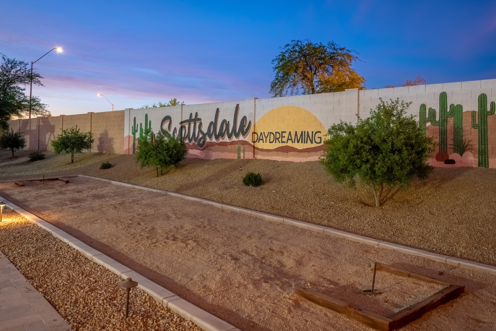 A painted wall sign marking the entrance to the Scottsdale Daydreaming area, surrounded by desert landscaping with cacti and native plants at dusk.