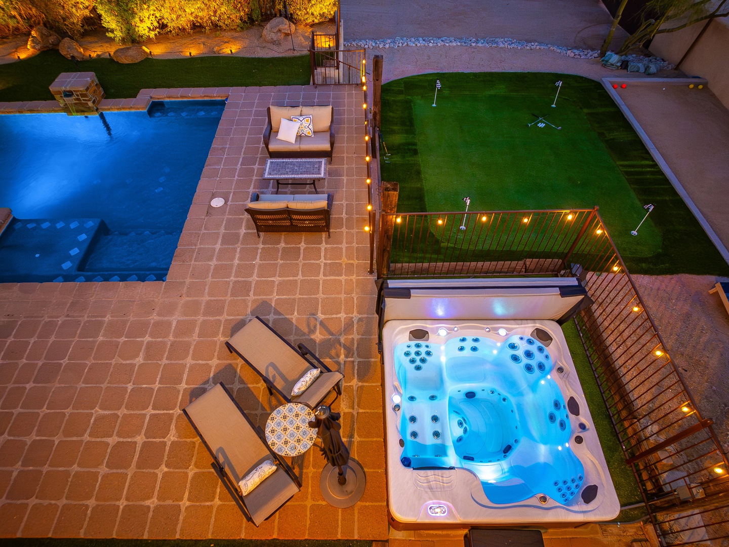 Aerial view of the property showcasing evening lighting with a blue pool, hot tub, putting green, and multiple outdoor seating and entertainment areas.